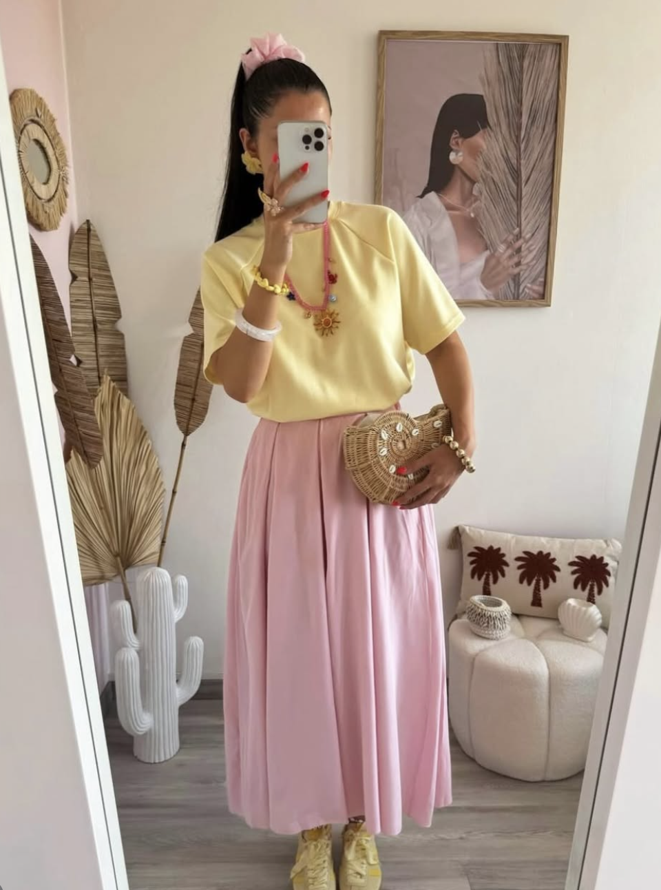 A woman taking a mirror selfie wearing a pale yellow button-down shirt and a large light pink hair bow.