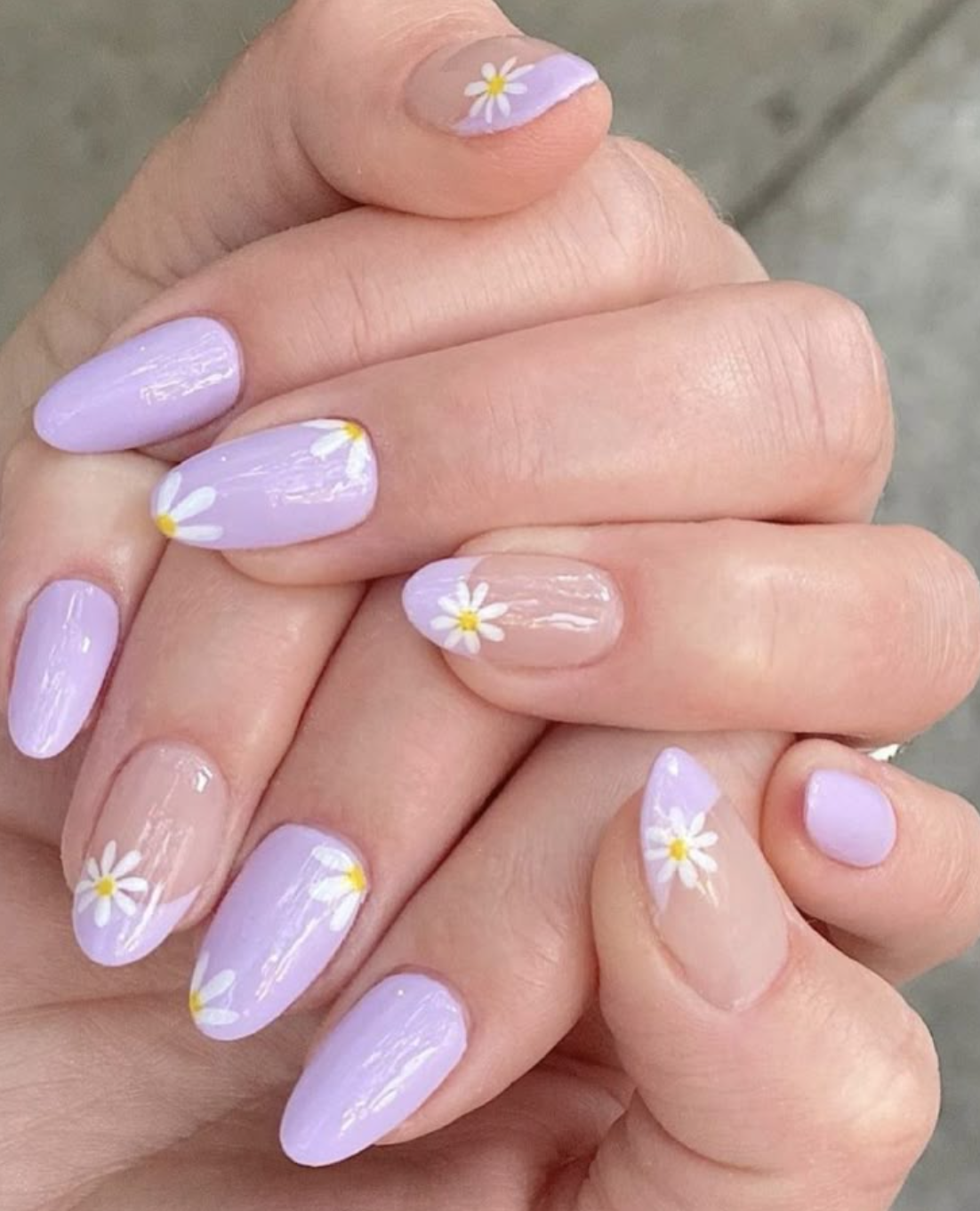 Oval-shaped lavender gel nails with accent nails featuring dainty white daisies on a sheer base.