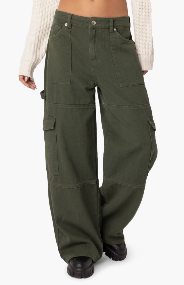 A close-up of a person wearing olive green denim cargo pants with large utility side pockets and black lug-sole boots.