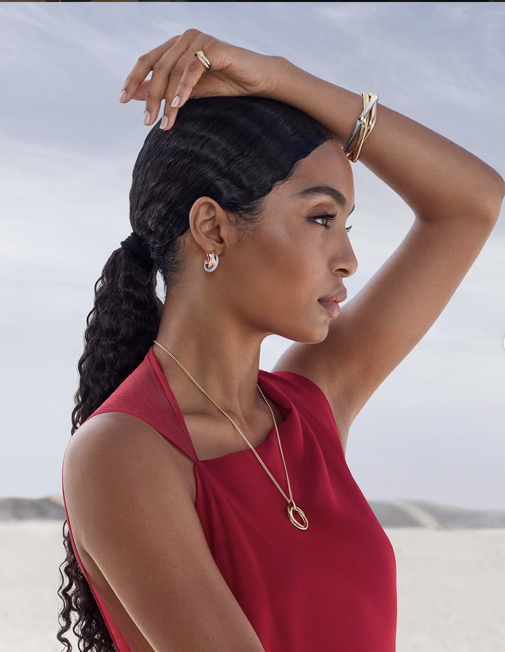 Yara Shahidi featuring a long, sleek jet-black wavy ponytail with a deep side part, wearing a red sleeveless top and gold jewelry.