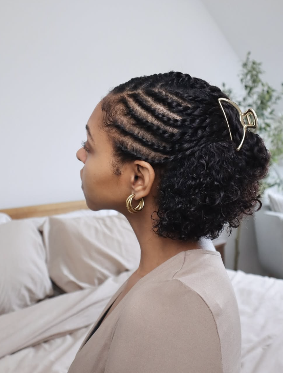 Side profile of a woman showcasing a half-up, half-down protective hairstyle with neat, crisp flat twists along the side of the head leading into a curly puff, accessorized with gold hoop earrings.