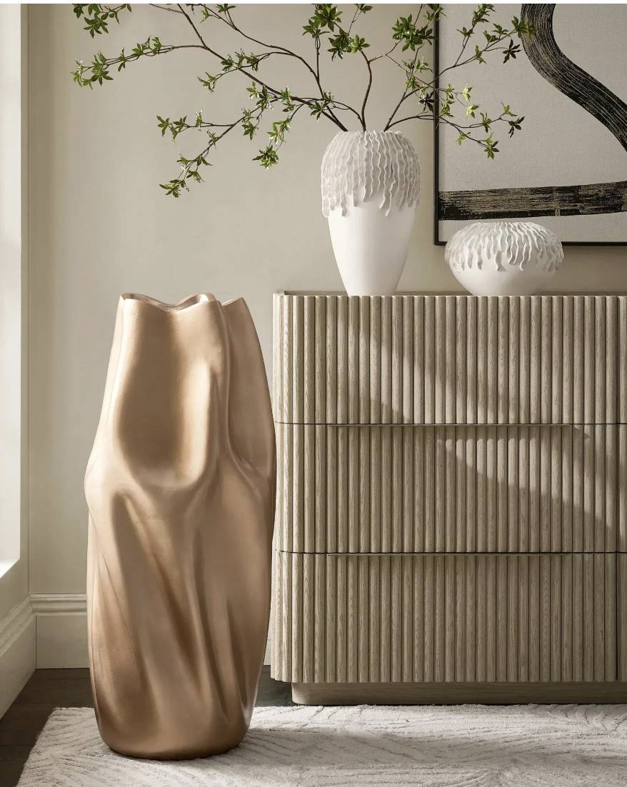 A modern neutral living room entry setup featuring a large off-white ceramic sculptural vase styled on a ribbed cream console table beside a large wall mirror.
