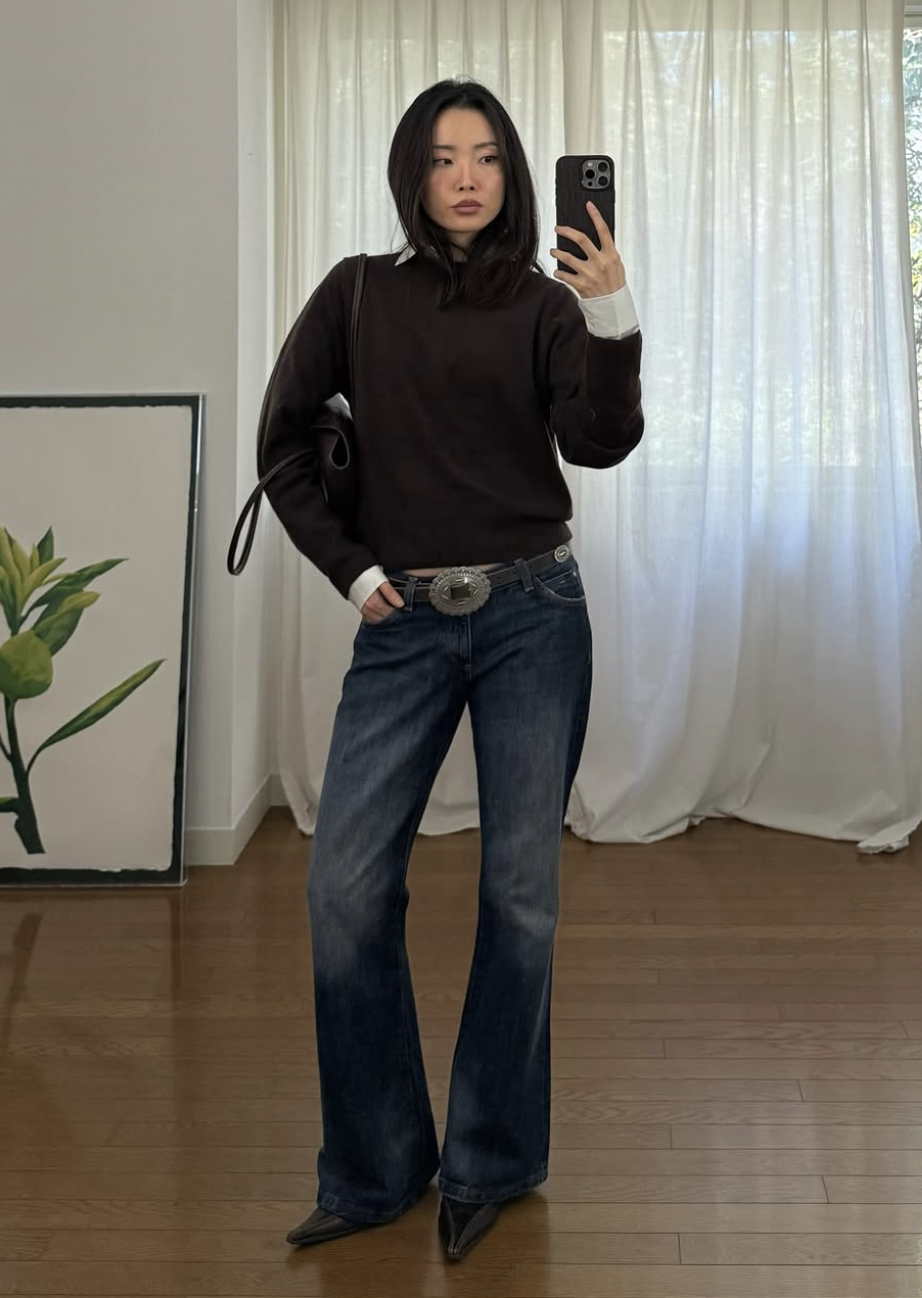 Fashion influencer Emma Jang wearing an oversized black sweater over a white collared shirt with dark wash bootcut jeans.