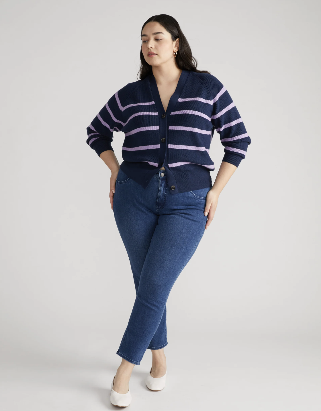 A person with an hourglass figure wearing dark blue Universal Standard Seine high-rise skinny jeans and a navy striped cardigan, highlighting a gap-free fit at the waist.