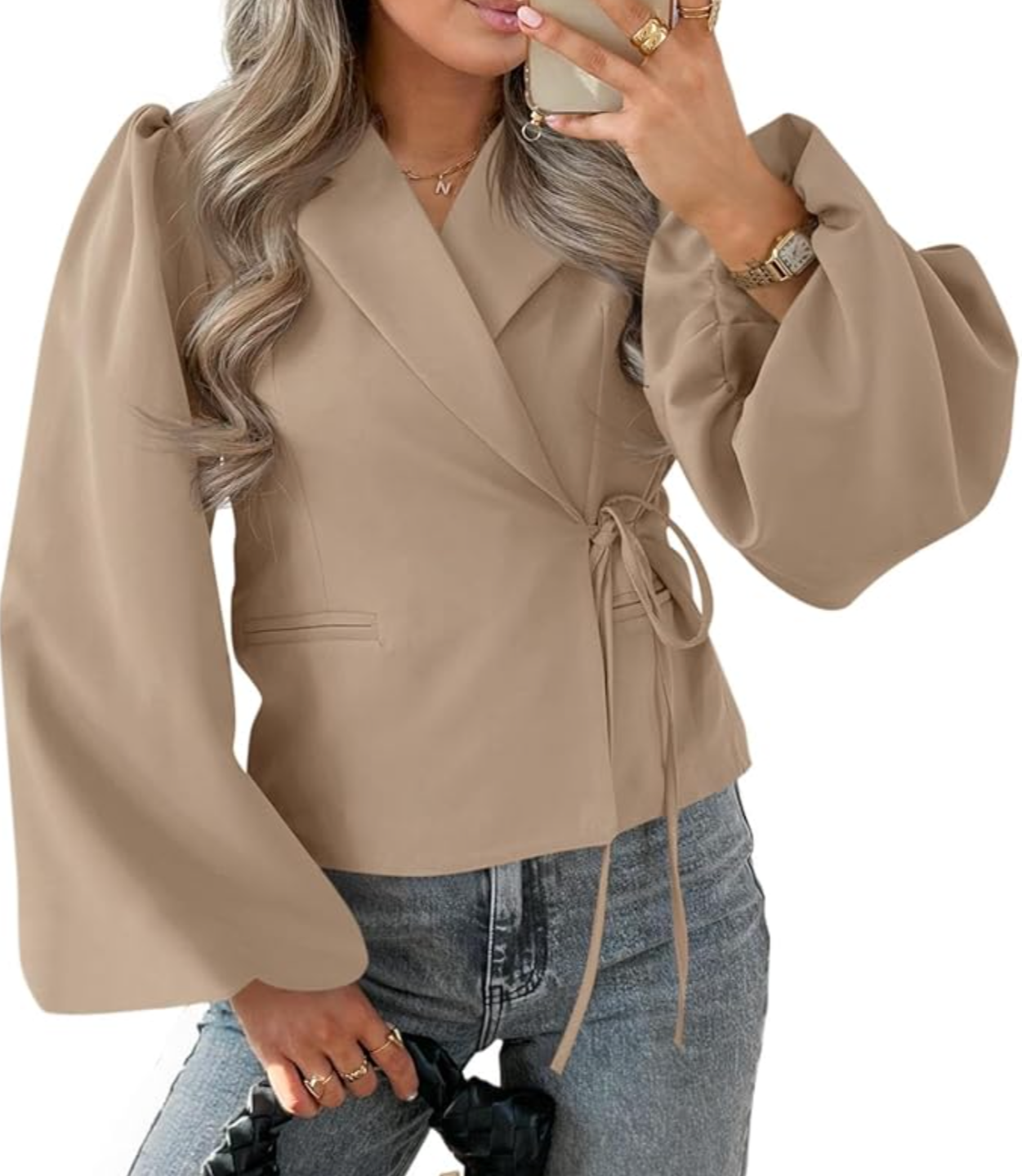 A studio product shot of a woman wearing a light beige long-sleeve blazer over a matching beige top and blue jeans, with her hands resting in her pockets.