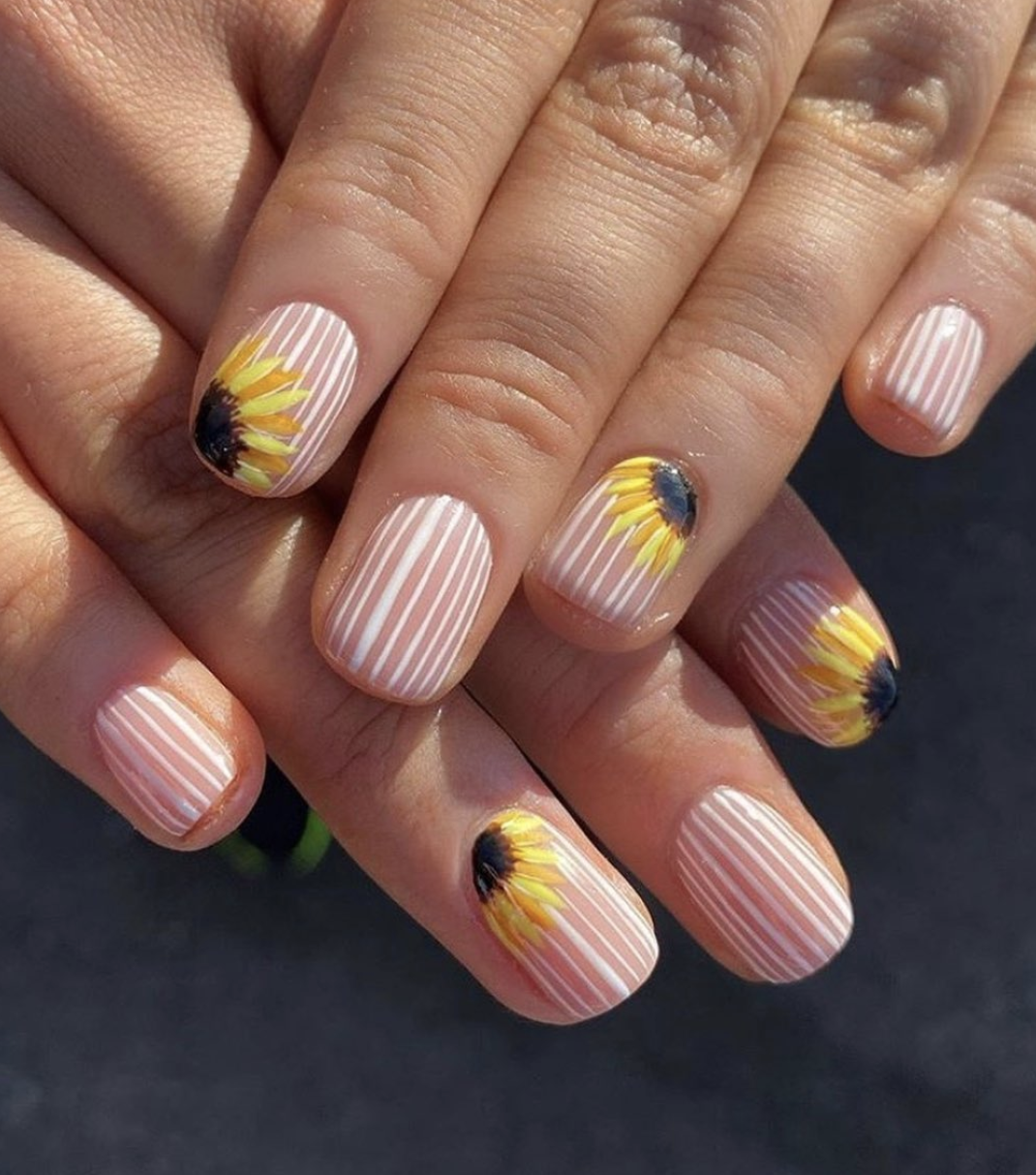 Close-up of almond-shaped nails featuring a white and nude vertical stripe pattern with large, detailed sunflowers painted over the stripes.