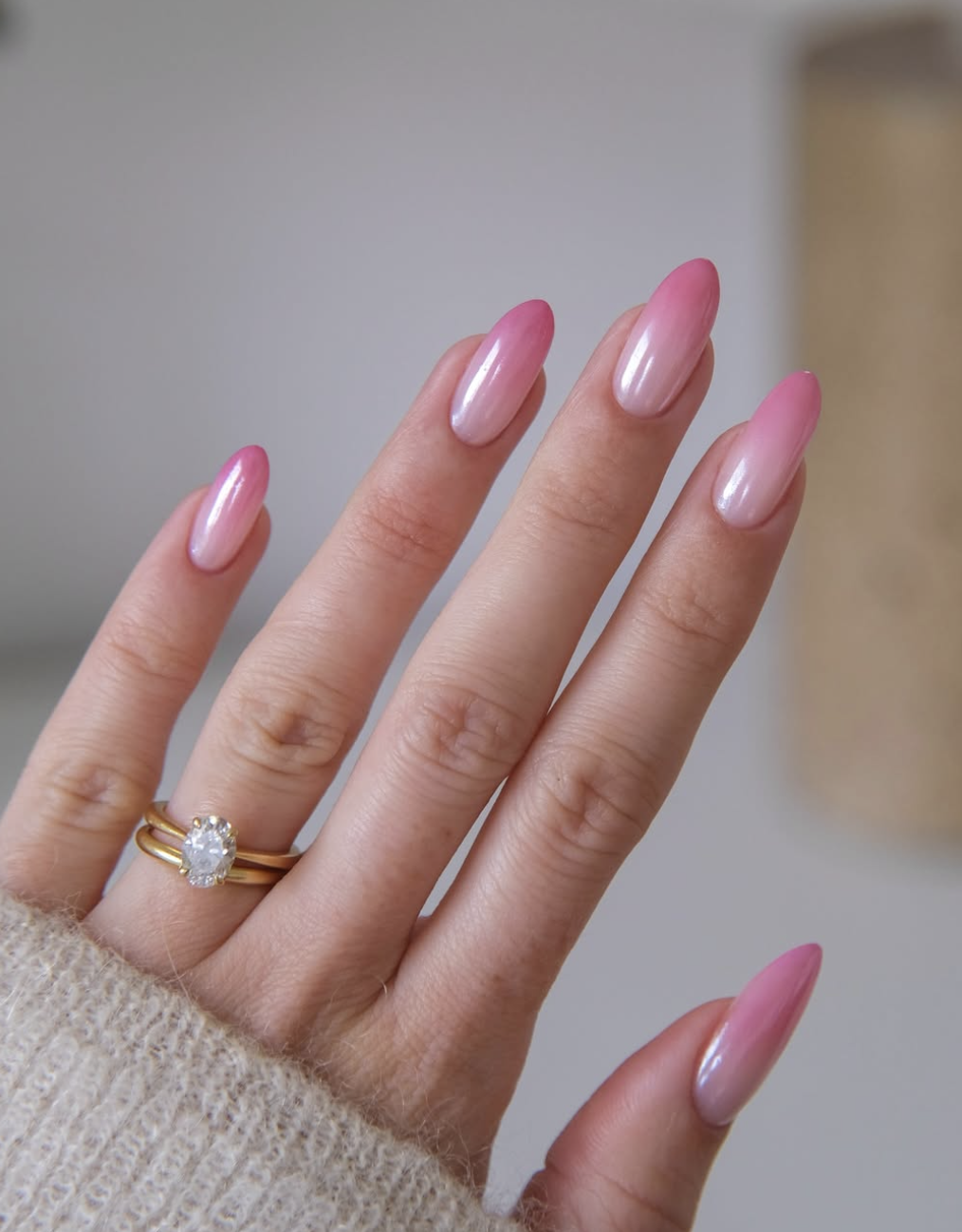 A close-up of long almond-shaped nails featuring a vertical pink ombré with a shimmering chrome finish.