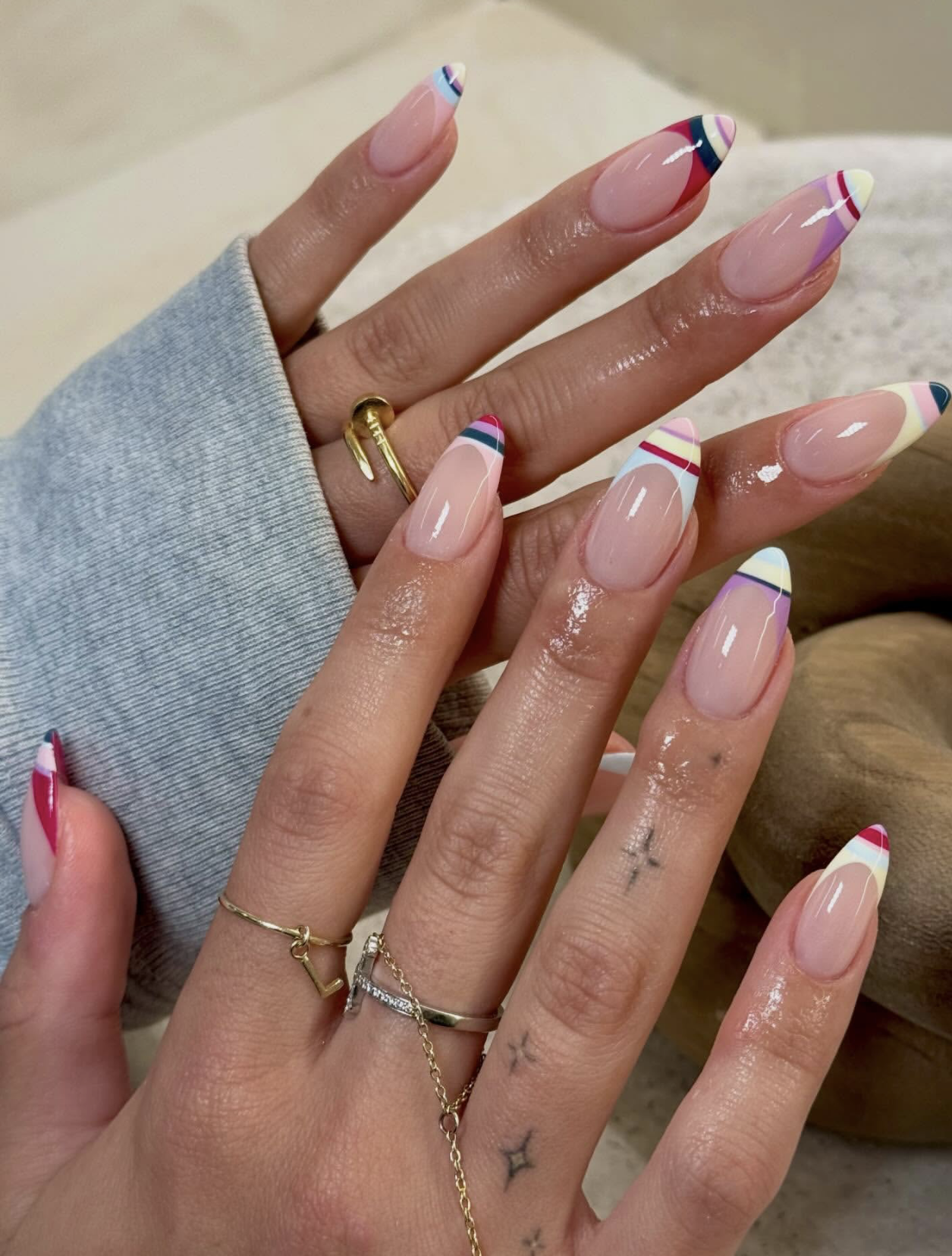 Long almond shaped nails with abstract geometric patterns in red, purple, blue, and cream.