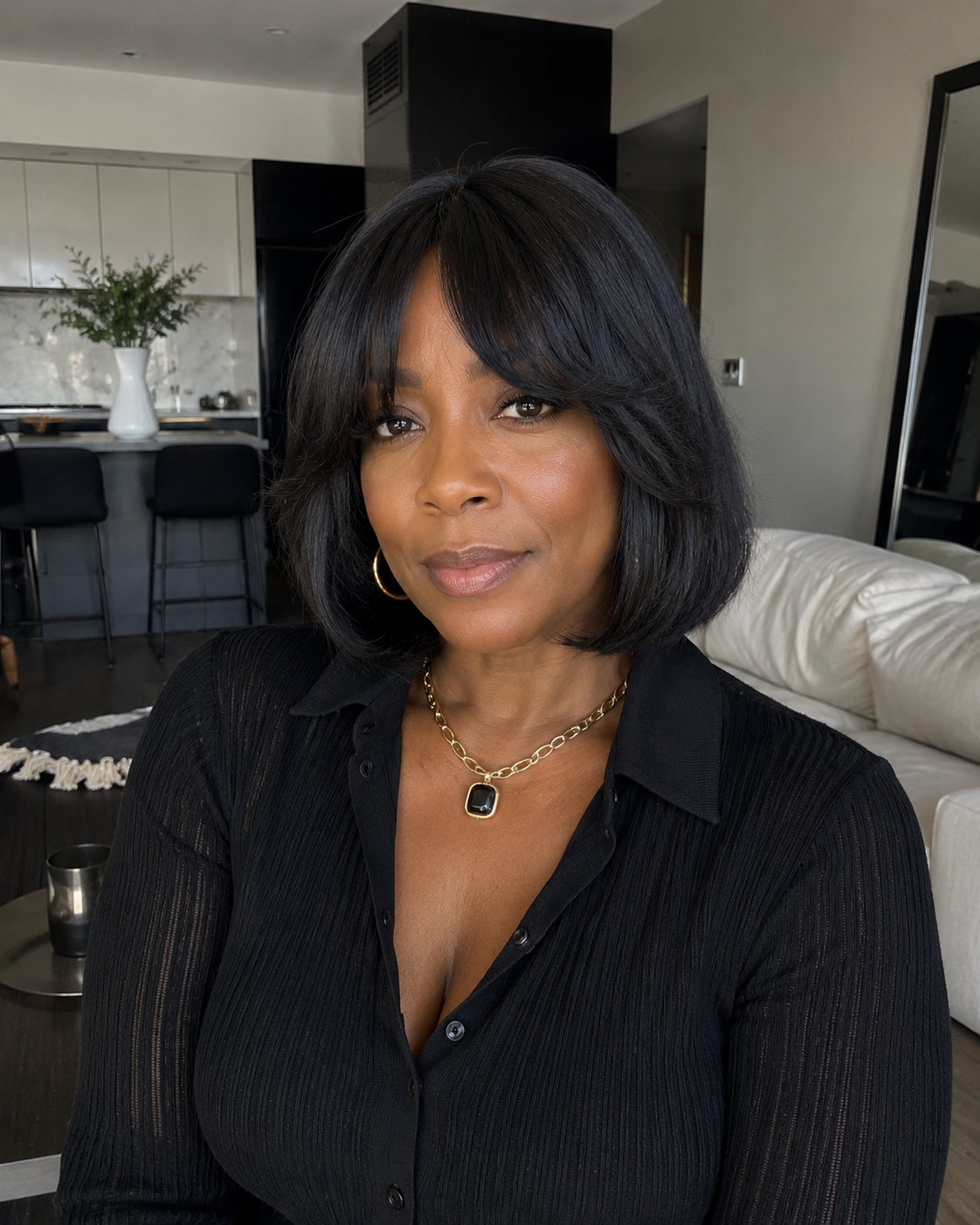 A chic woman over 50 with a modern, sleek chin-length black bob haircut and face-framing curtain bangs.