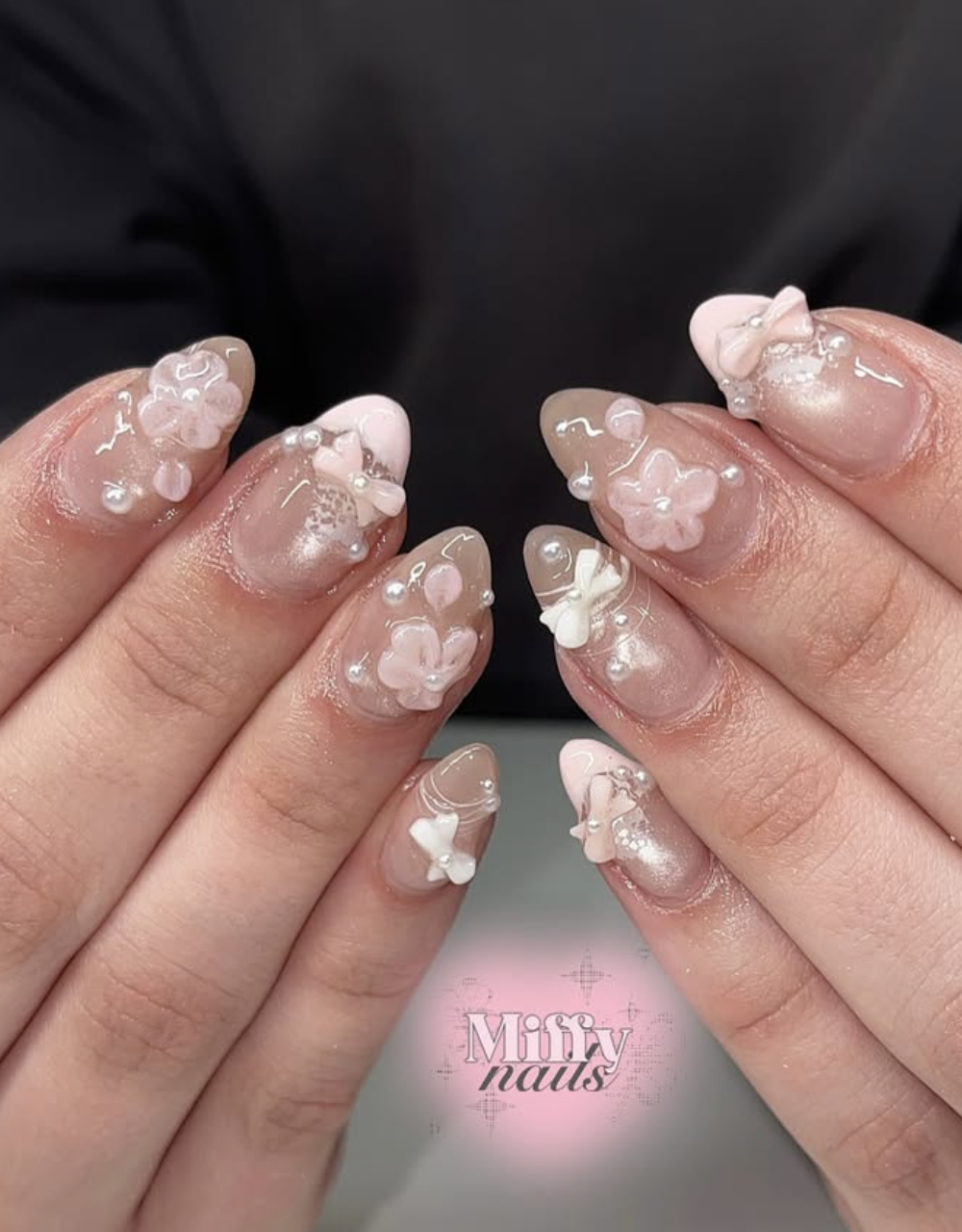 Long almond-shaped nails with a sheer nude base featuring 3D white resin bow charms, delicate white floral accents, and scattered pearl details.
