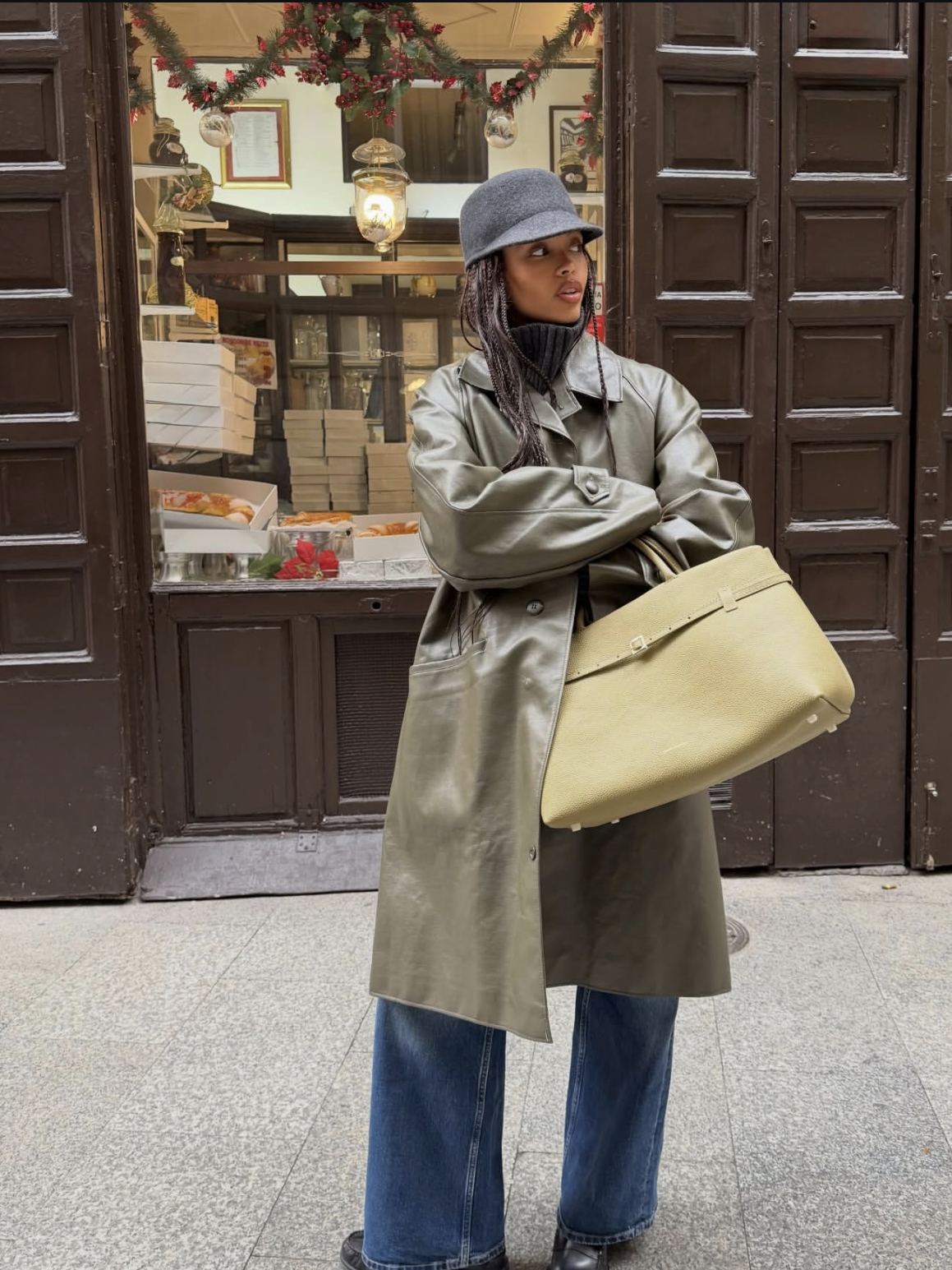 A woman wearing a grey coat, grey beanie, and blue straight-leg jeans styled with black Mary Jane flats for women while holding a cream tote bag.