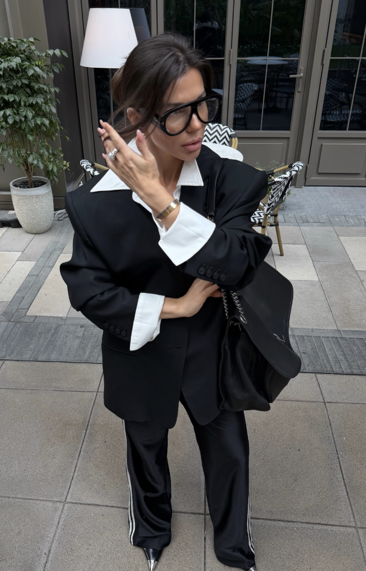 A professional Corporate Sport outfit featuring black Adidas track pants with white stripes, paired with a sharp black structured blazer and silver pointed-toe heels for a modern office look.