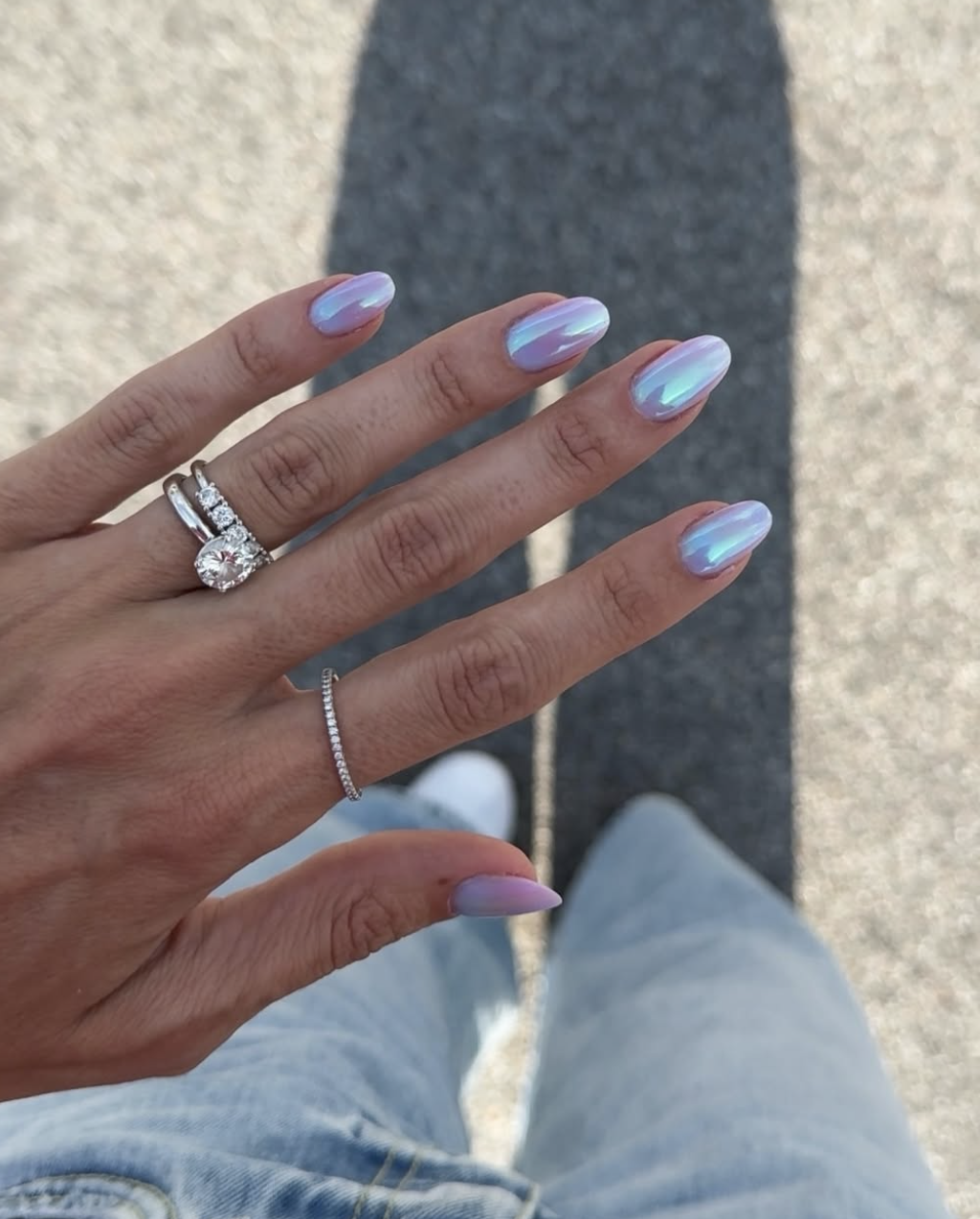 A close-up of almond-shaped nails with a cool-toned light pink and lavender iridescent chrome finish.