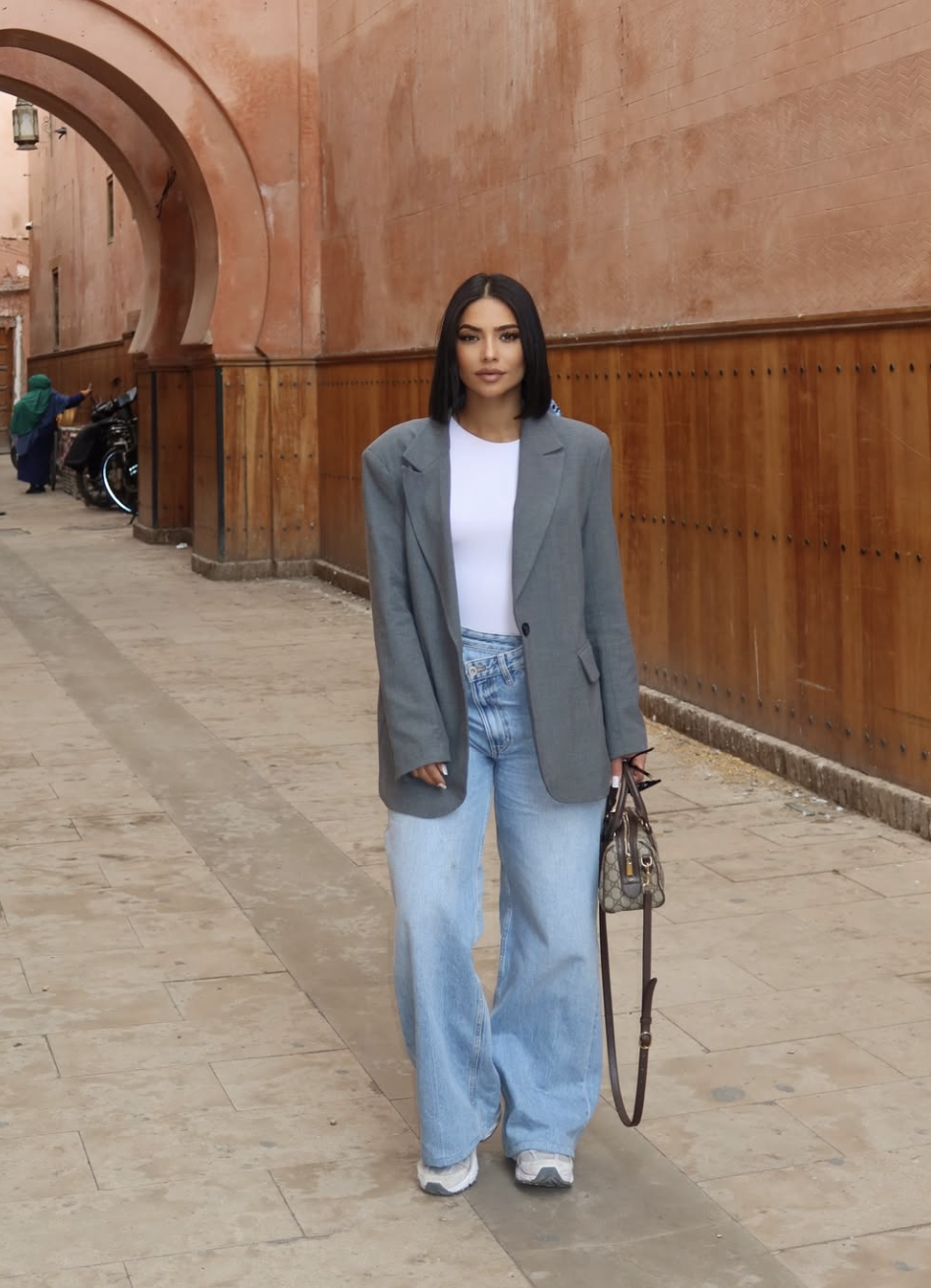 A woman wearing light-wash baggy jeans with a fitted white tee and a structured grey tailored blazer to demonstrate a professional yet relaxed outfit formula.