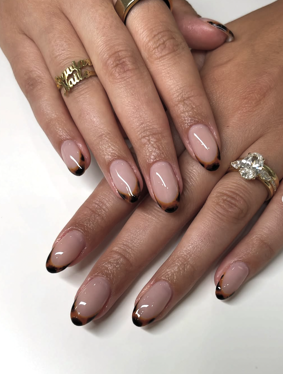 Close-up of short nails featuring a tortoiseshell micro French tip with amber and brown patterned edges over a sheer nude pink base.