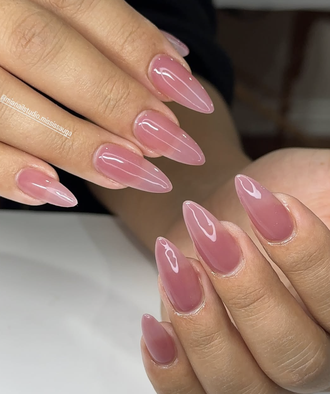 Close-up of a hand with long, stiletto-shaped nails showcasing a glossy, translucent pink jelly manicure that has a candy-like, see-through finish.