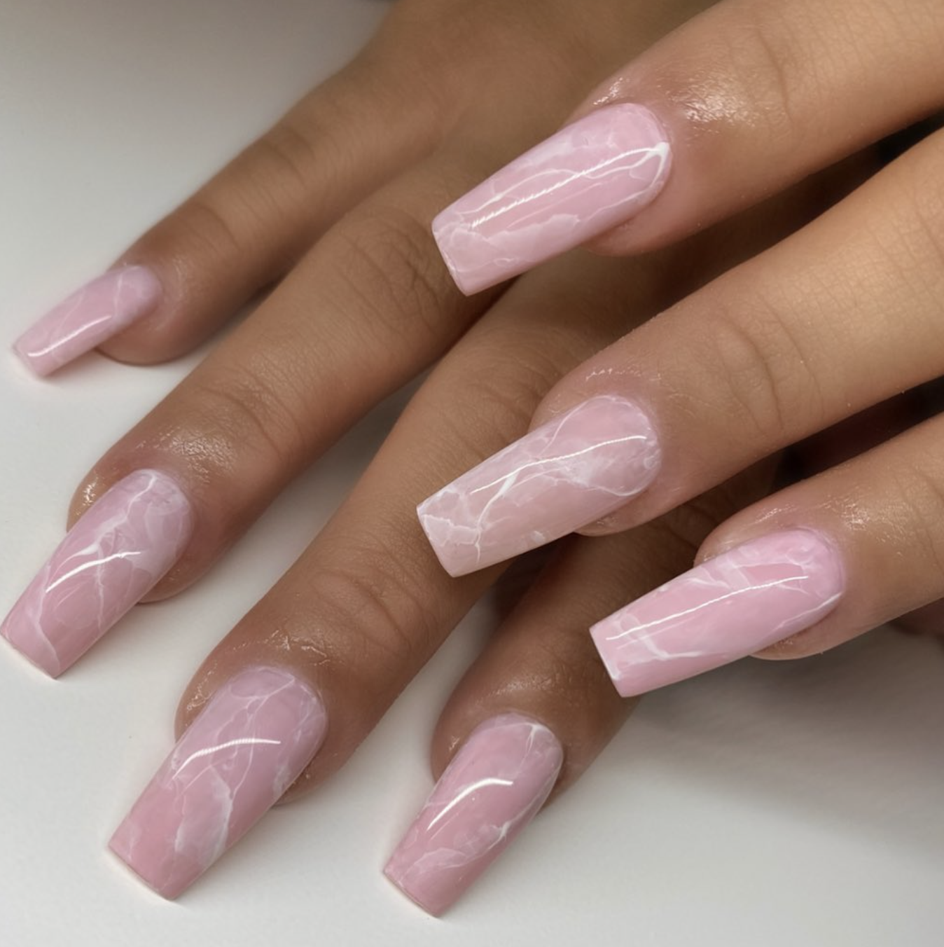 Long coffin-shaped gel nails with a soft pink and white marble pattern featuring delicate rose-gold veining.