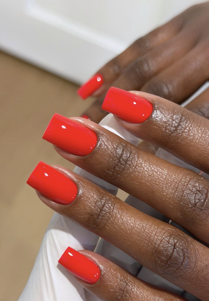 A close-up of short, softly rounded nails with a glossy, vibrant cherry red nail polish manicure.