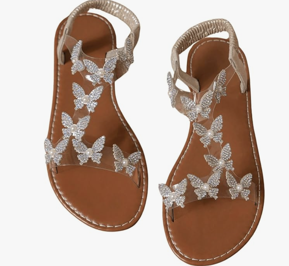 A pair of Butterfly Transparent clear flat sandals with tan soles and decorative sparkling butterfly accents on the straps, styled for a summer BBQ outfit.