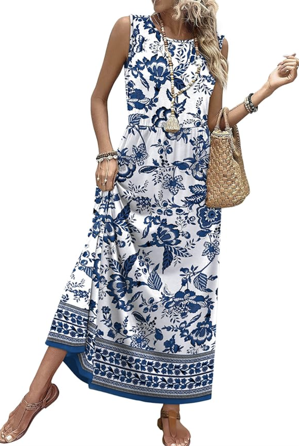 A woman wearing a sleeveless blue and white floral print maxi dress with a tiered skirt, styled as a versatile travel-ready piece for a Spring capsule wardrobe for women in their 50s.