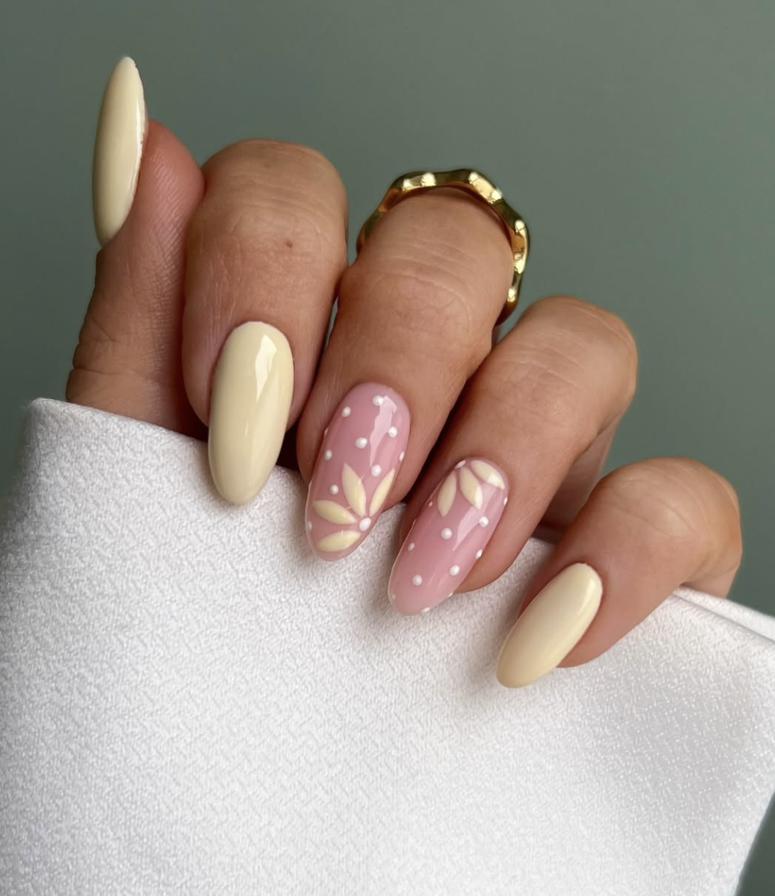 A high-feminine spring manicure by @iolapallade_beauty featuring almond-shaped nails in butter yellow and soft pink with hand-painted white flowers and dainty polka dots.