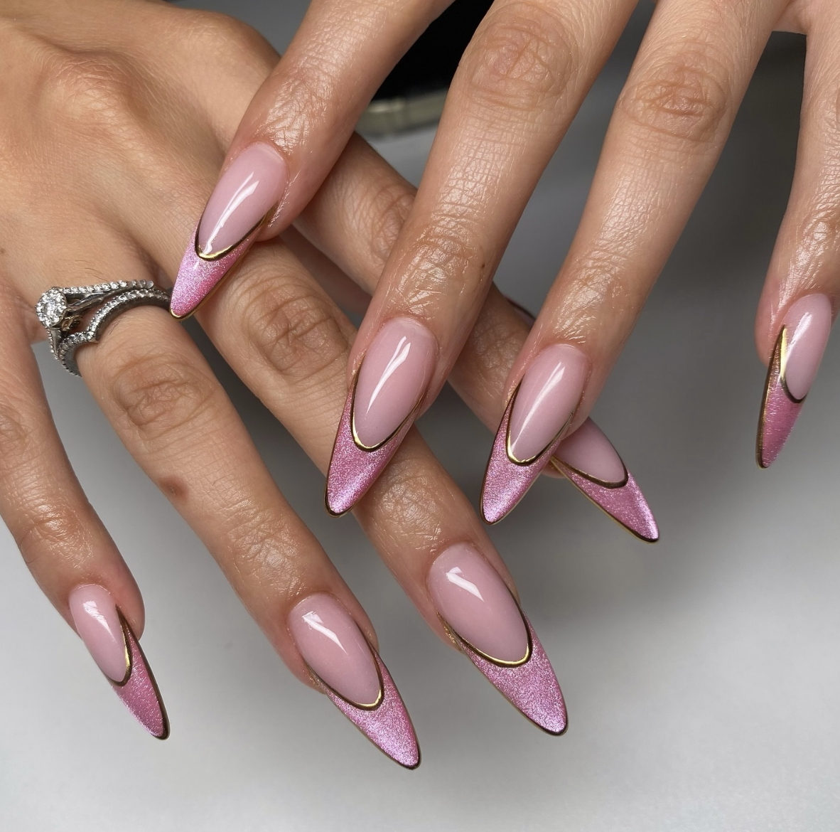 A close-up of tapered nails with a light pink chrome finish and a delicate gold metallic outline around the edges.