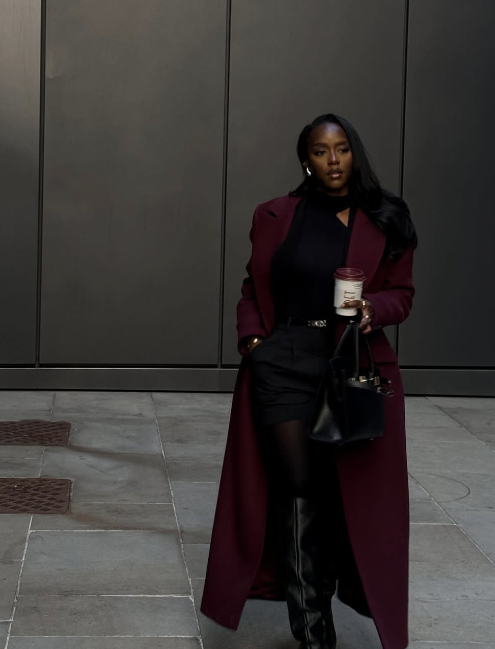 A woman wearing a dark brown structured blazer, a black beret, and a tie, leaning against a stone pillar to showcase the poetcore aesthetic.
