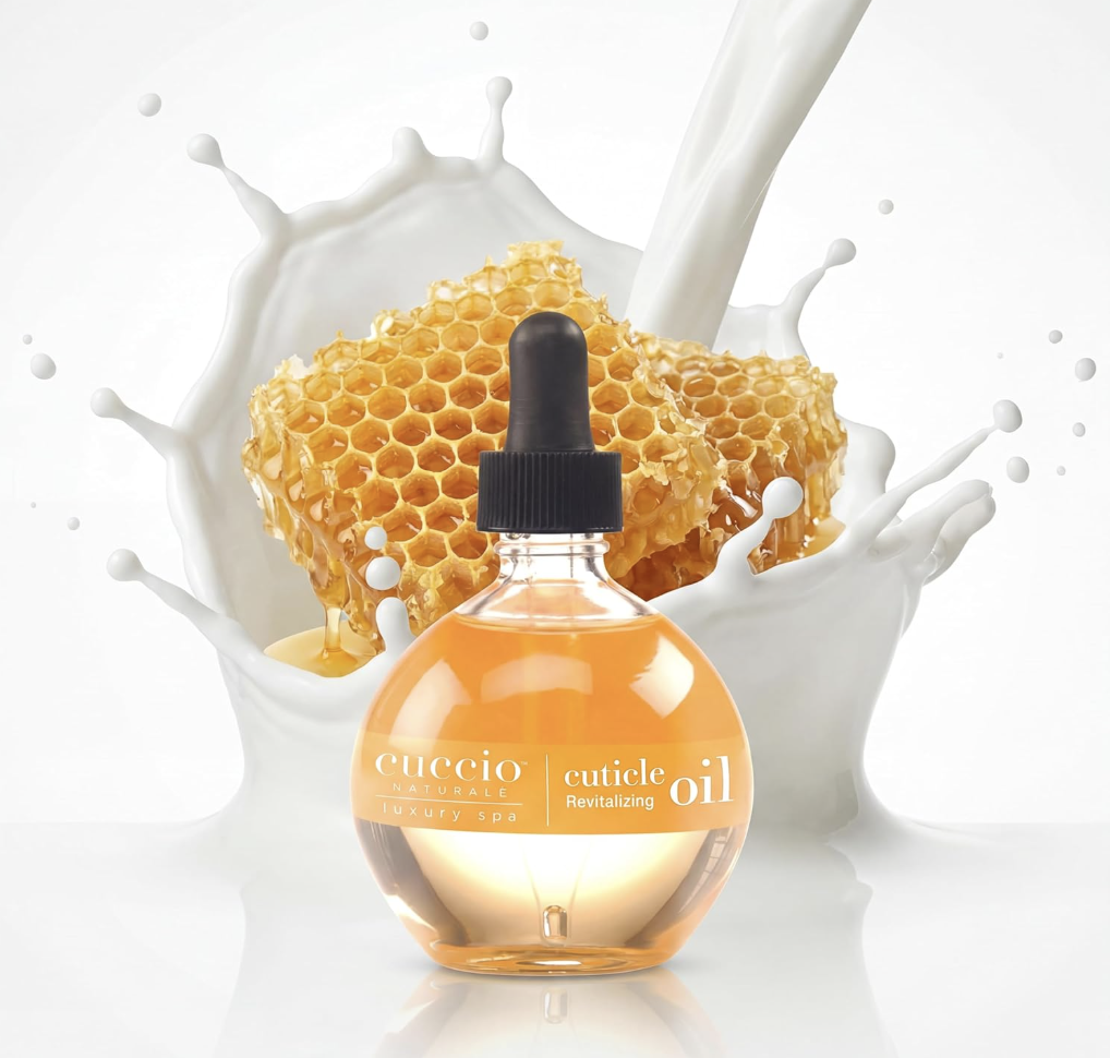 A bottle of Cuccio Naturale Milk and Honey Revitalizing Cuticle Oil with a dropper, featuring honeycombs and splashing milk in the background.