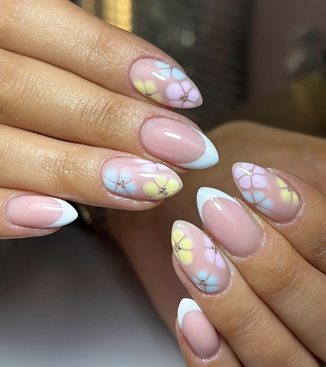 Almond-shaped French tip nails with delicate hand-painted pastel flowers and tiny silver stud centers.