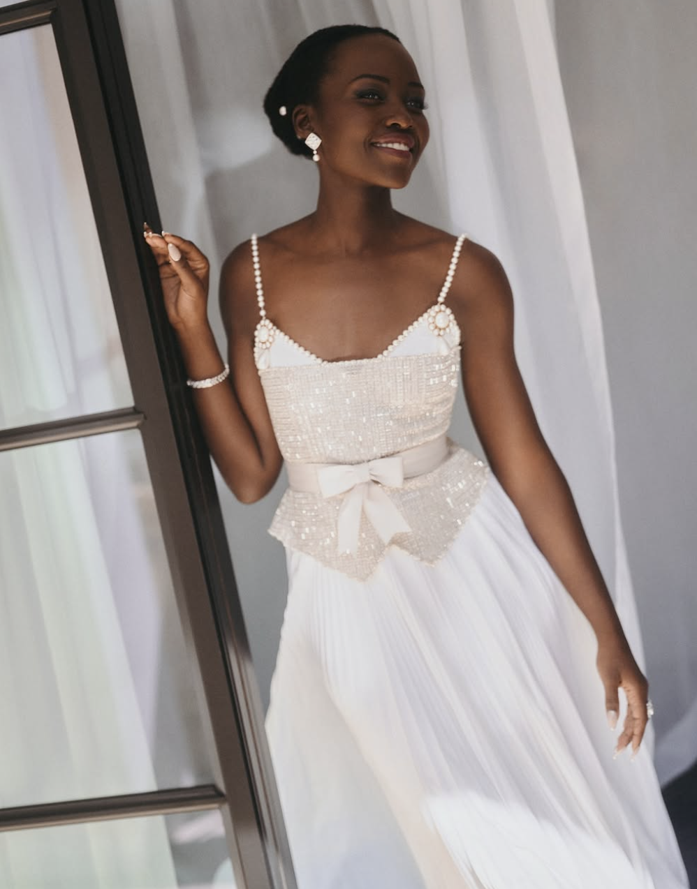 Lupita Nyong'o wearing a soft, warm-neutral cream dress with pearl detailing, illustrating how muted, earthy undertones harmonize with the Soft Autumn season.