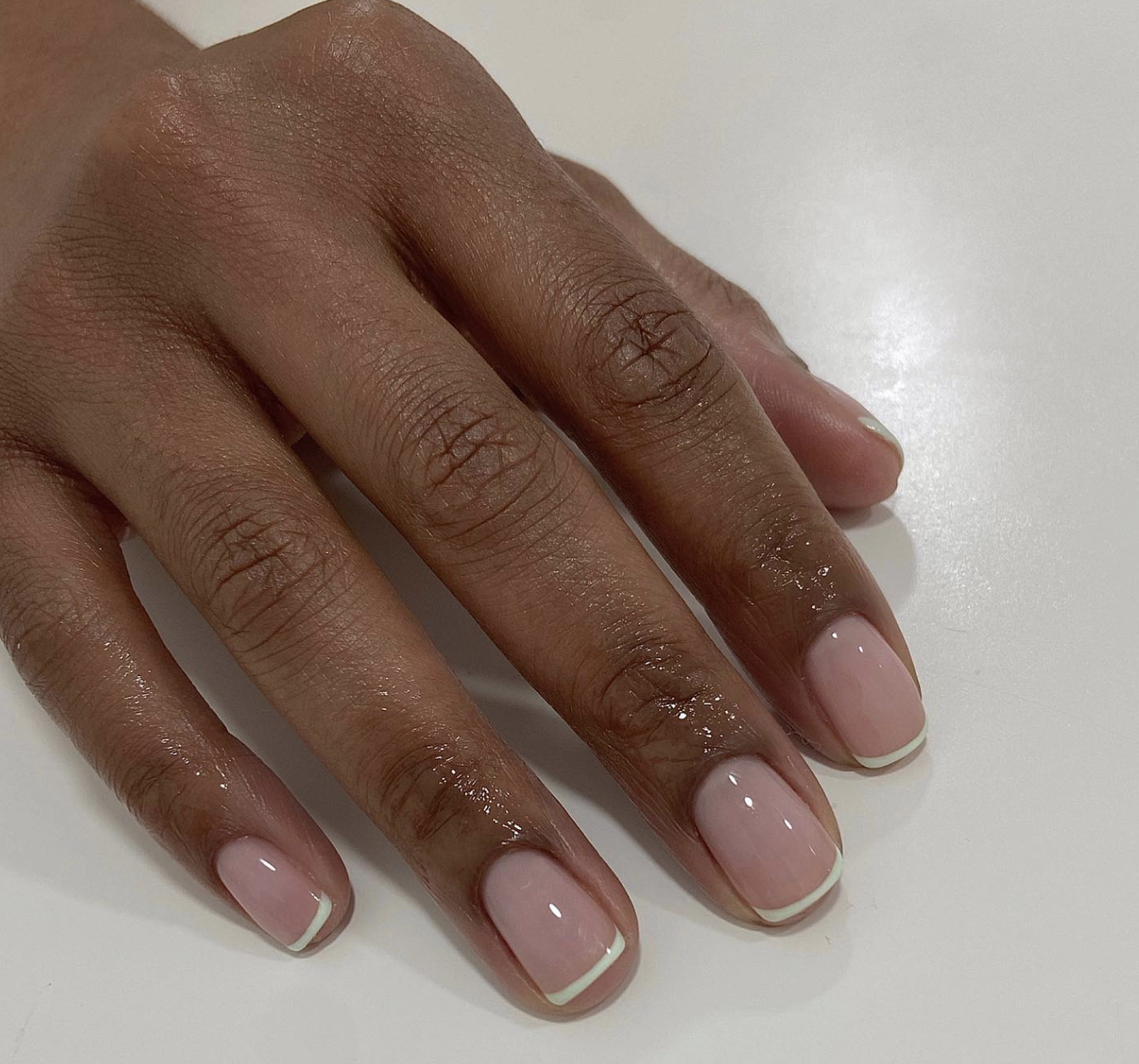 A close-up of a short, square-shaped micro French manicure featuring ultra-thin mint green tips on a sheer pink base.