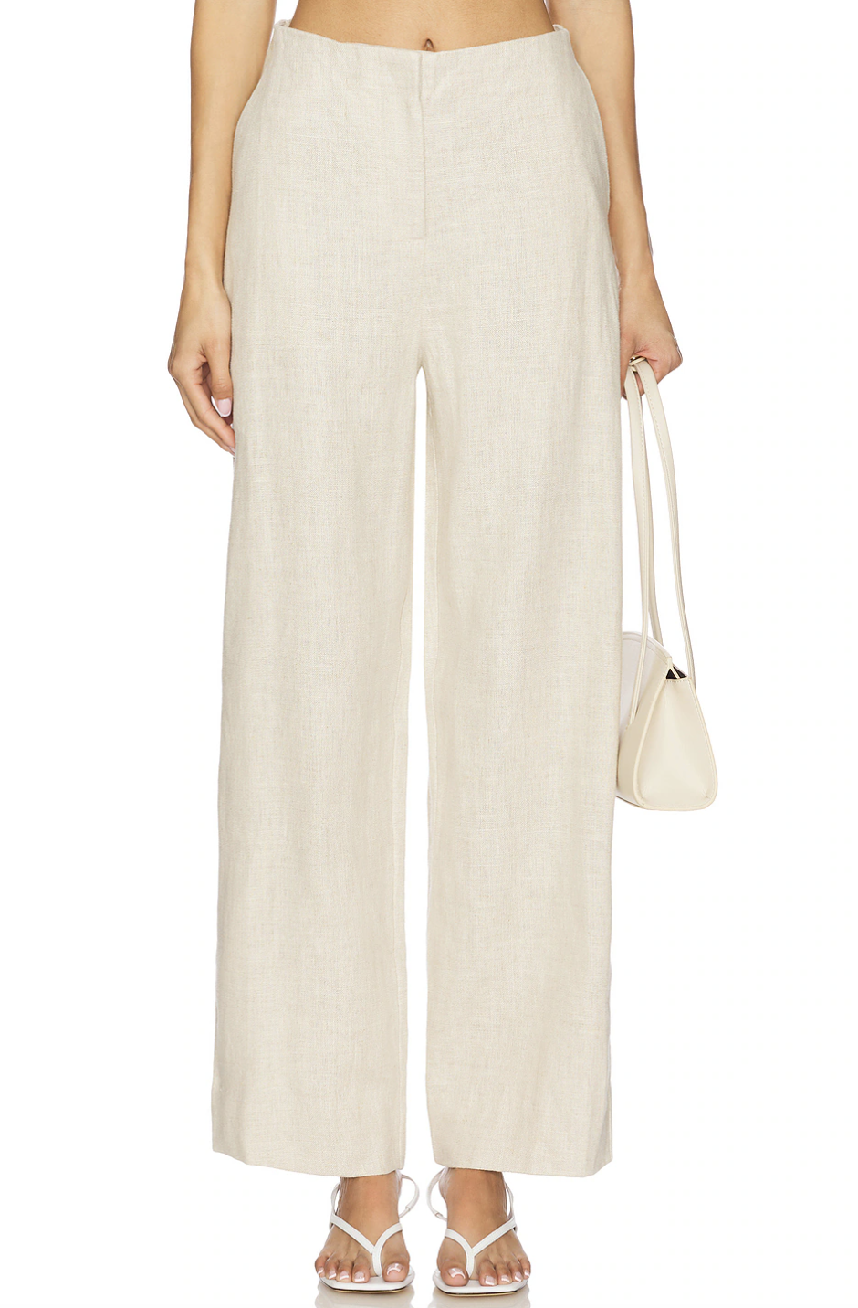 A close-up view of a woman wearing cream-colored, high-waisted, wide-leg linen trousers and holding a small cream shoulder bag.