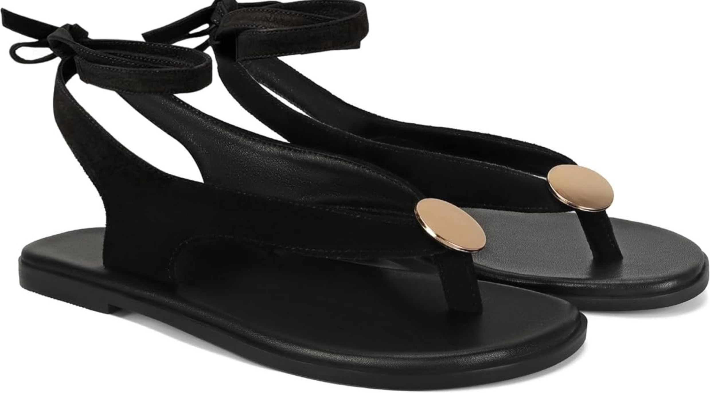 A pair of black strappy thong sandals with a gold coin embellishment, a lightweight footwear choice for styling white linen pants or white cropped jeans.