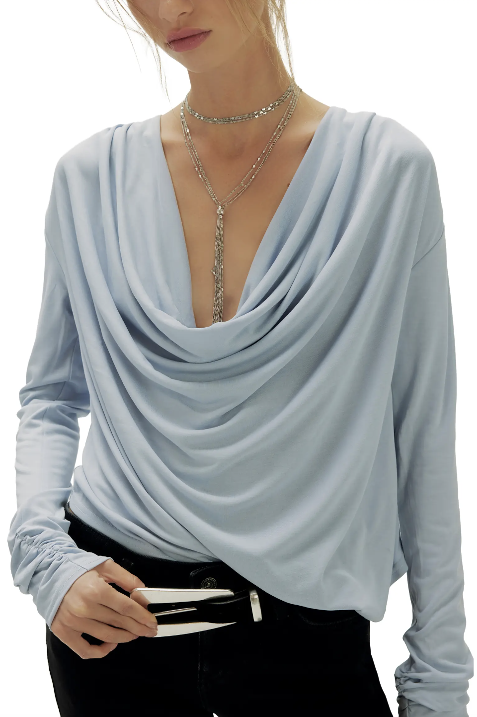 A woman wearing a soft light blue long-sleeve draped cowl-neck blouse styled with delicate layered necklaces.