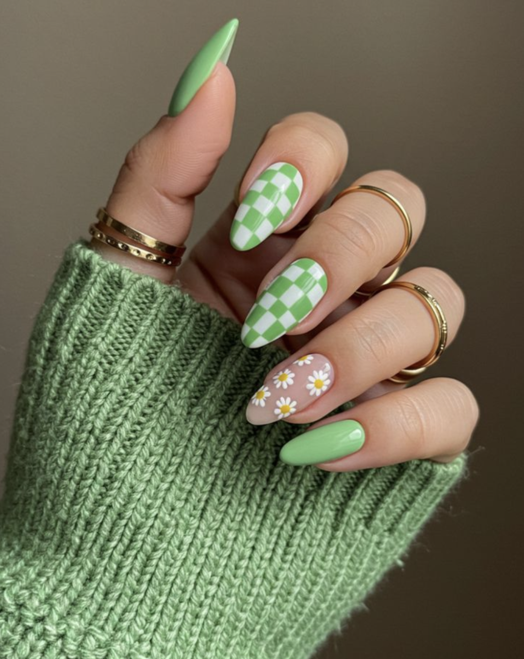 Almond-shaped nails featuring a mix of light green and white checkerboard patterns and hand-painted white daisy nail art.
