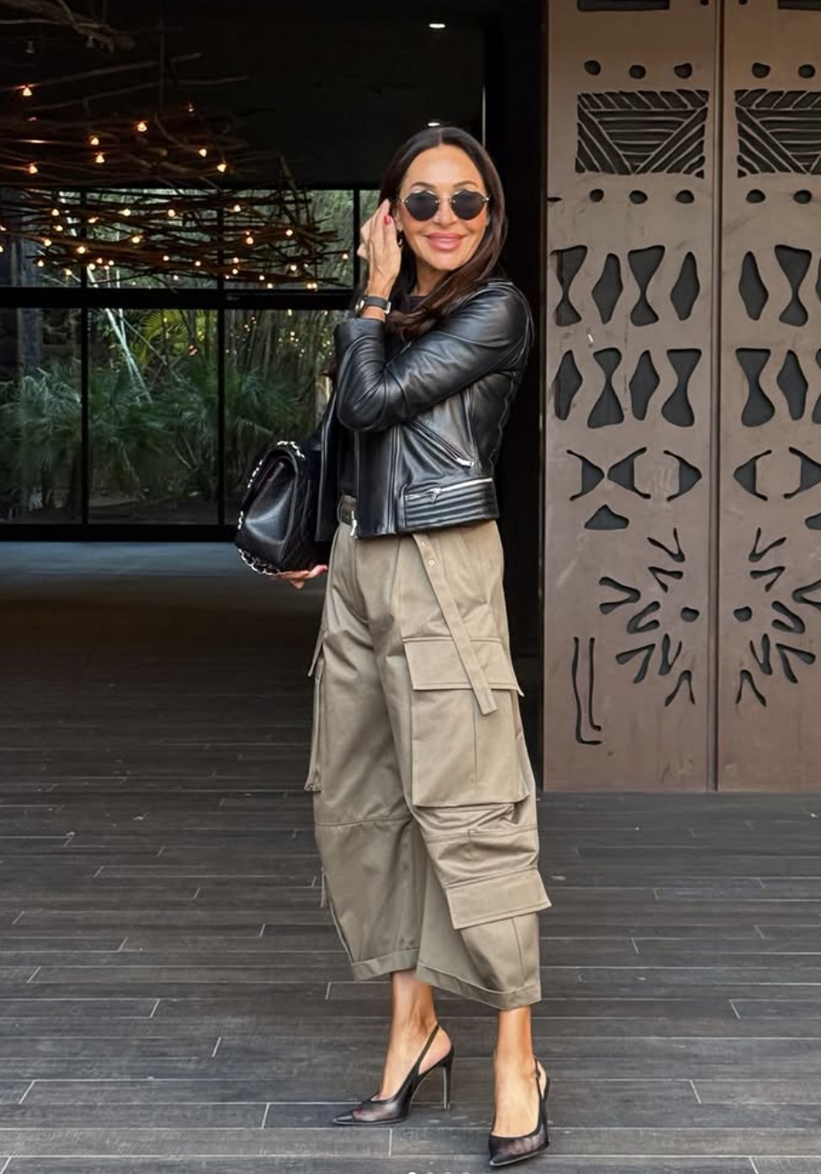 A person wearing khaki wide-leg cargo pants paired with a black leather corset-style jacket and pointed-toe slingback heels.
