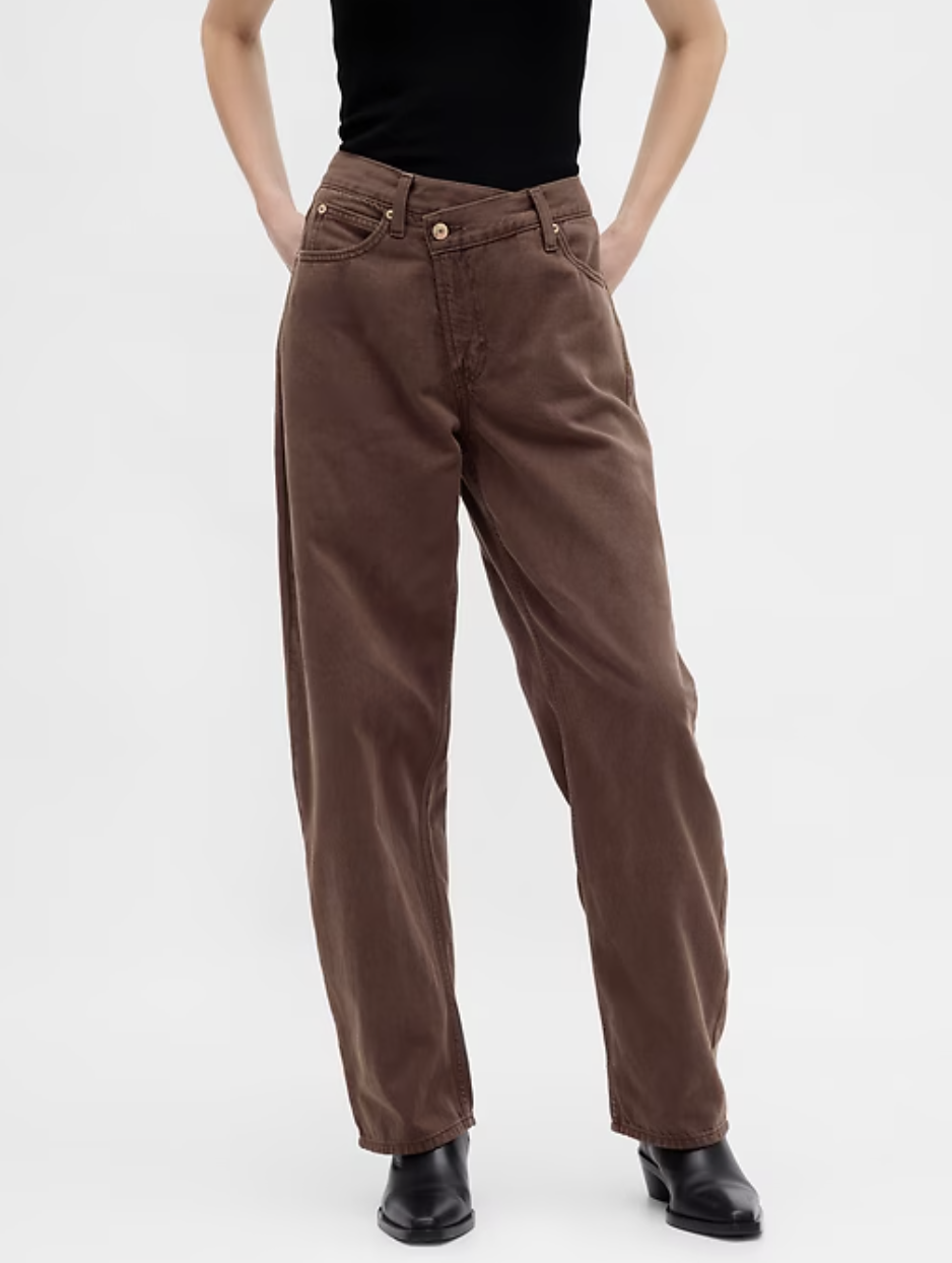 A person wearing brown high-waisted barrel jeans with a unique crossover waistband and a relaxed, tapered leg.