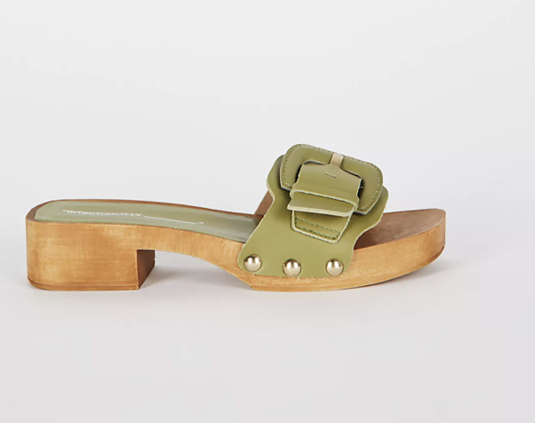 A side profile product shot of a light lime green leather slip-on clog sandal featuring an oversized adjustable top strap with a matching leather buckle, a flat light wood sole, and gold stud accents.