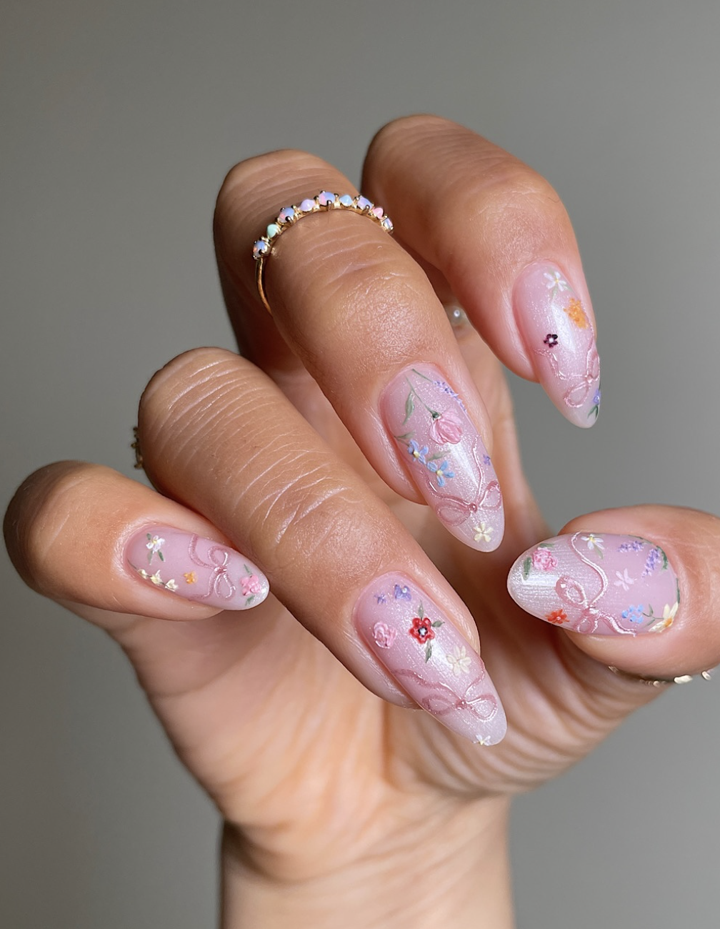 Long almond-shaped nails with a sheer pink base featuring delicate hand-painted floral designs and tiny pink bow accents.
