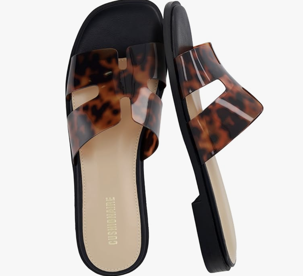 A pair of faux-leather slide sandals featuring a brown and black tortoise shell pattern with a cutout H-strap design and a tan cushioned sole.