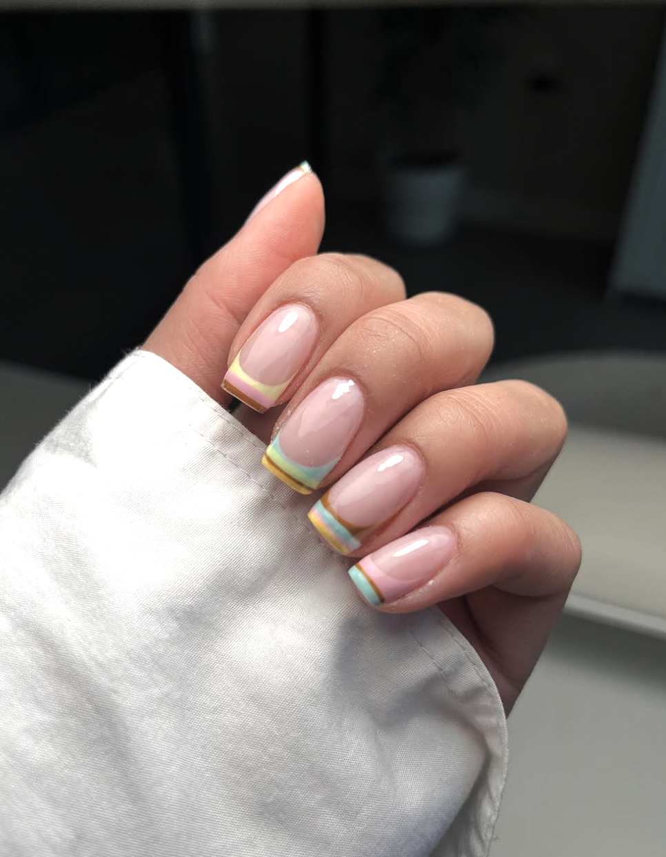 A close-up of a short nail French manicure featuring delicate pastel blue and peach tips on a clean, natural base.