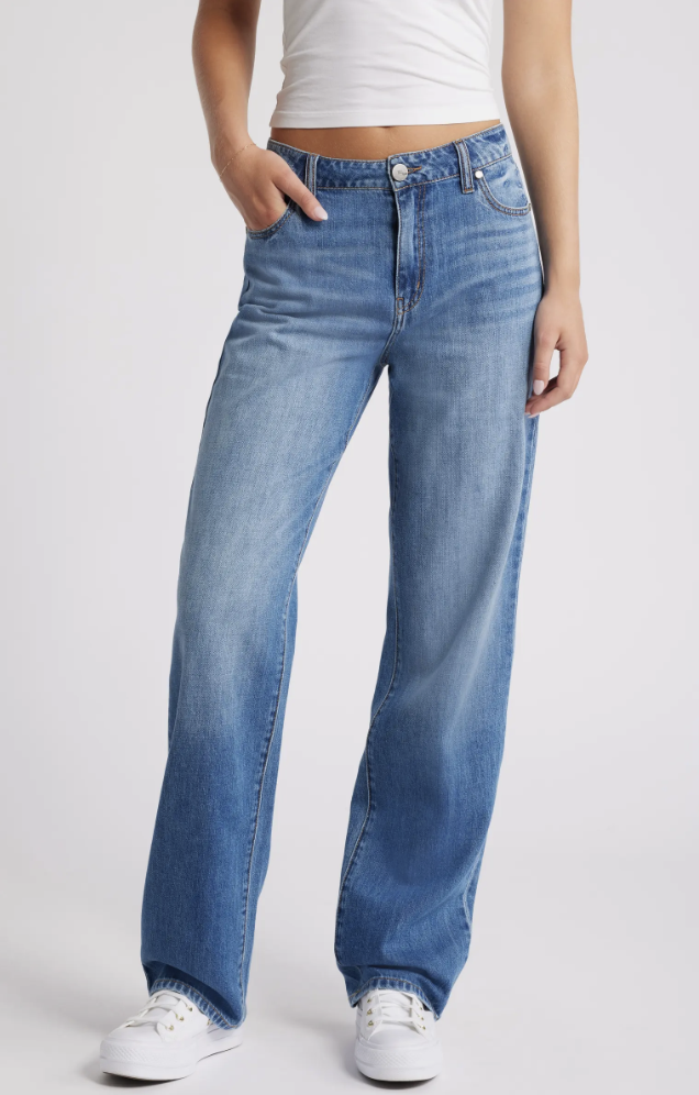 A woman wearing 1822 Denim high-waist baggy straight-leg jeans in a light blue wash with a white cropped tank top.