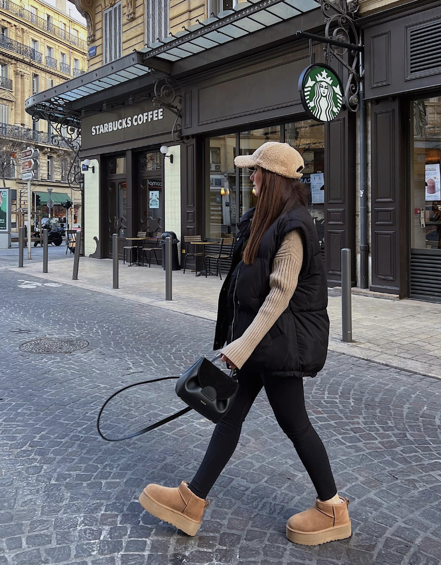 Black puffer vest over a beige ribbed sweater with black leggings and chestnut platform boots.