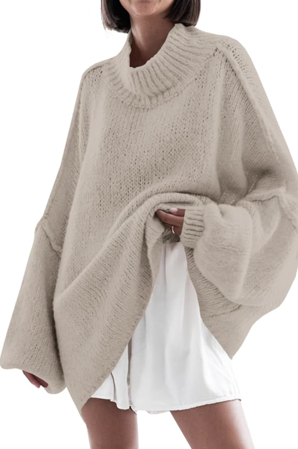A woman wearing an oversized, chunky beige knit sweater with wide sleeves over a white dress or skirt.