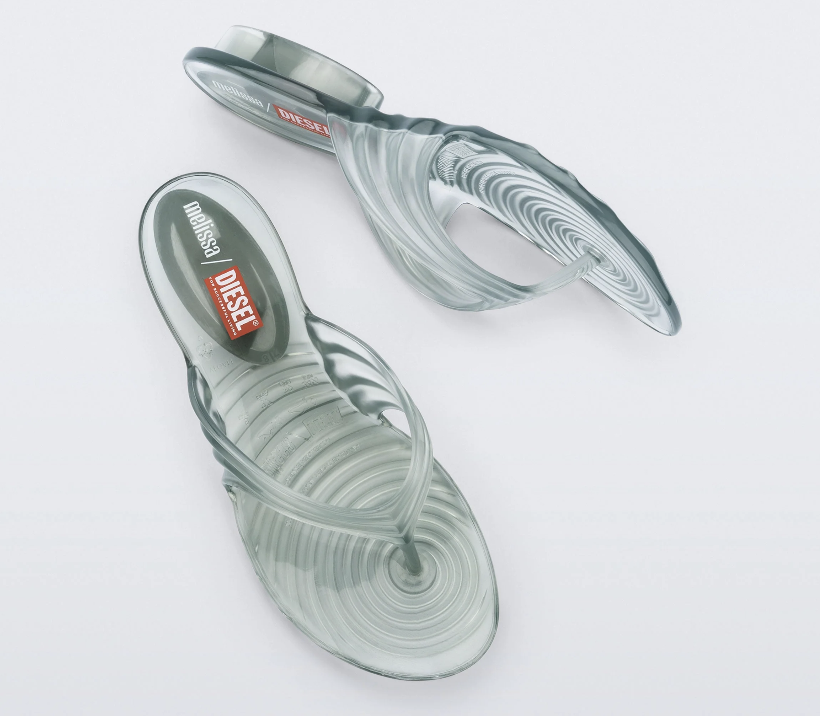 A close-up product view of a clear, translucent grey jelly thong sandal showcasing a prominent Diesel logo printed on the red and black footbed cushioned insole.