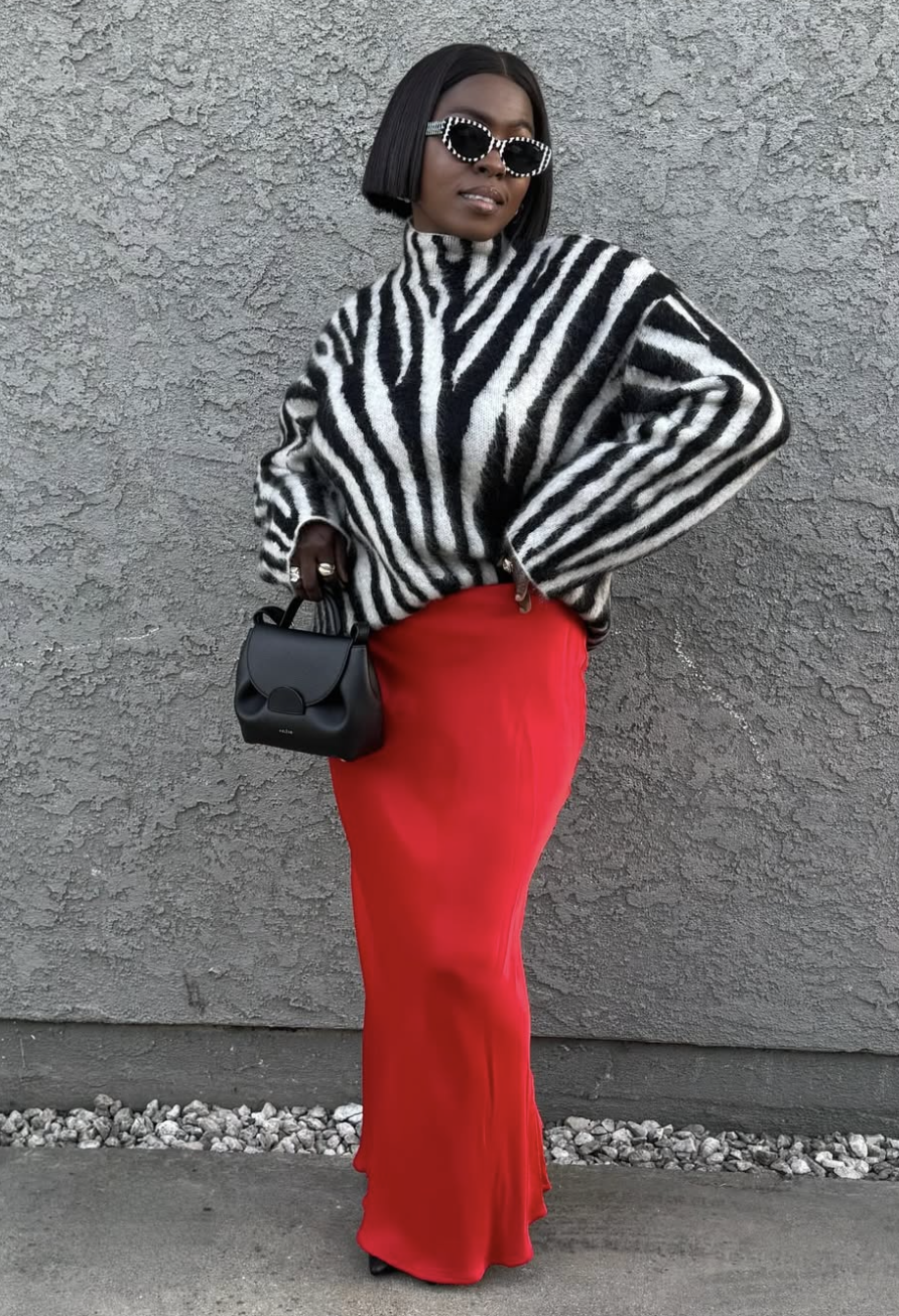 A woman wearing an oversized black and white zebra-print sweater paired with a high-waisted red satin maxi skirt and a black handbag.