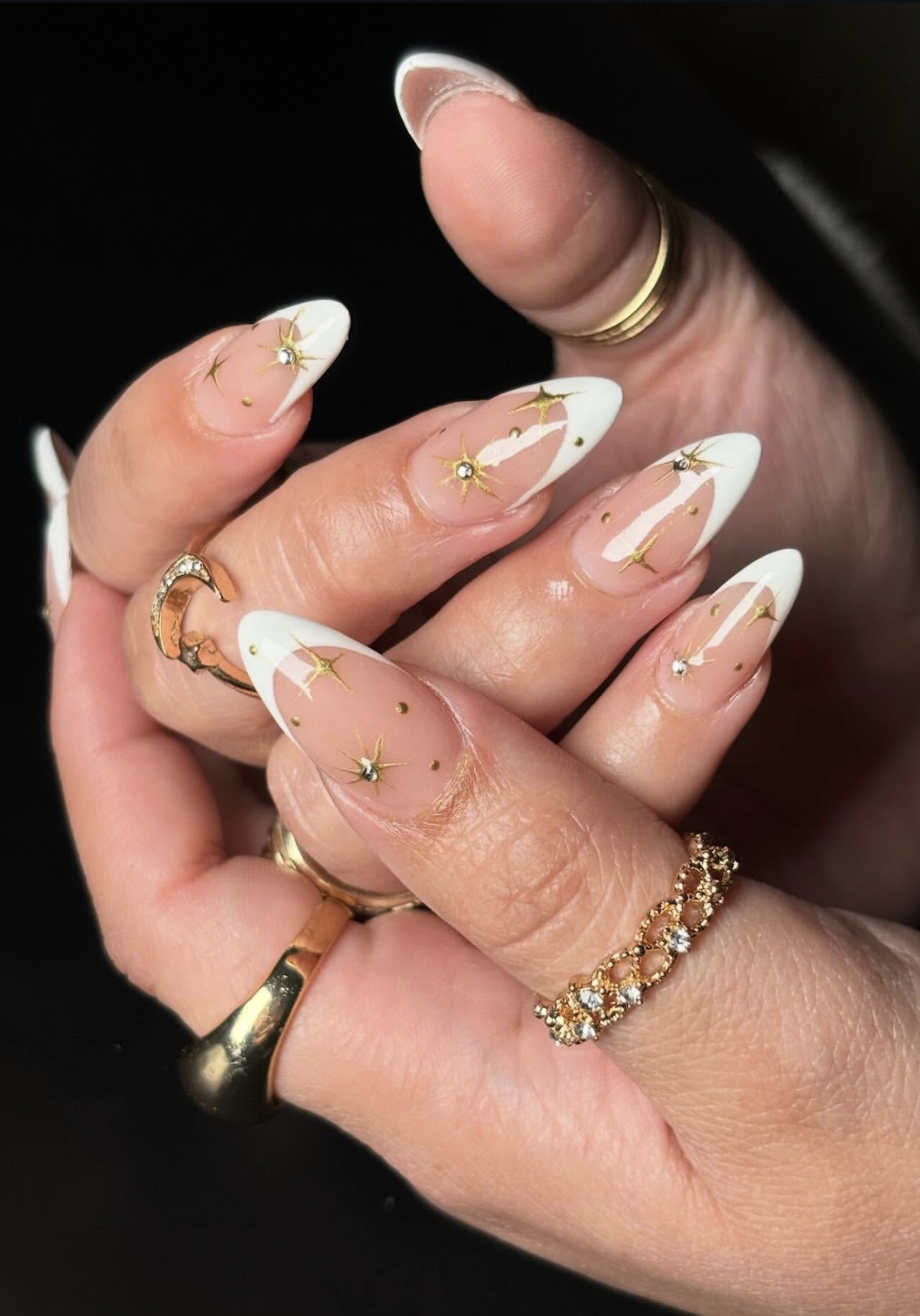 Long, almond-shaped nails featuring a crisp white French manicure base upgraded with delicate hand-painted gold starbursts and tiny metallic dots.