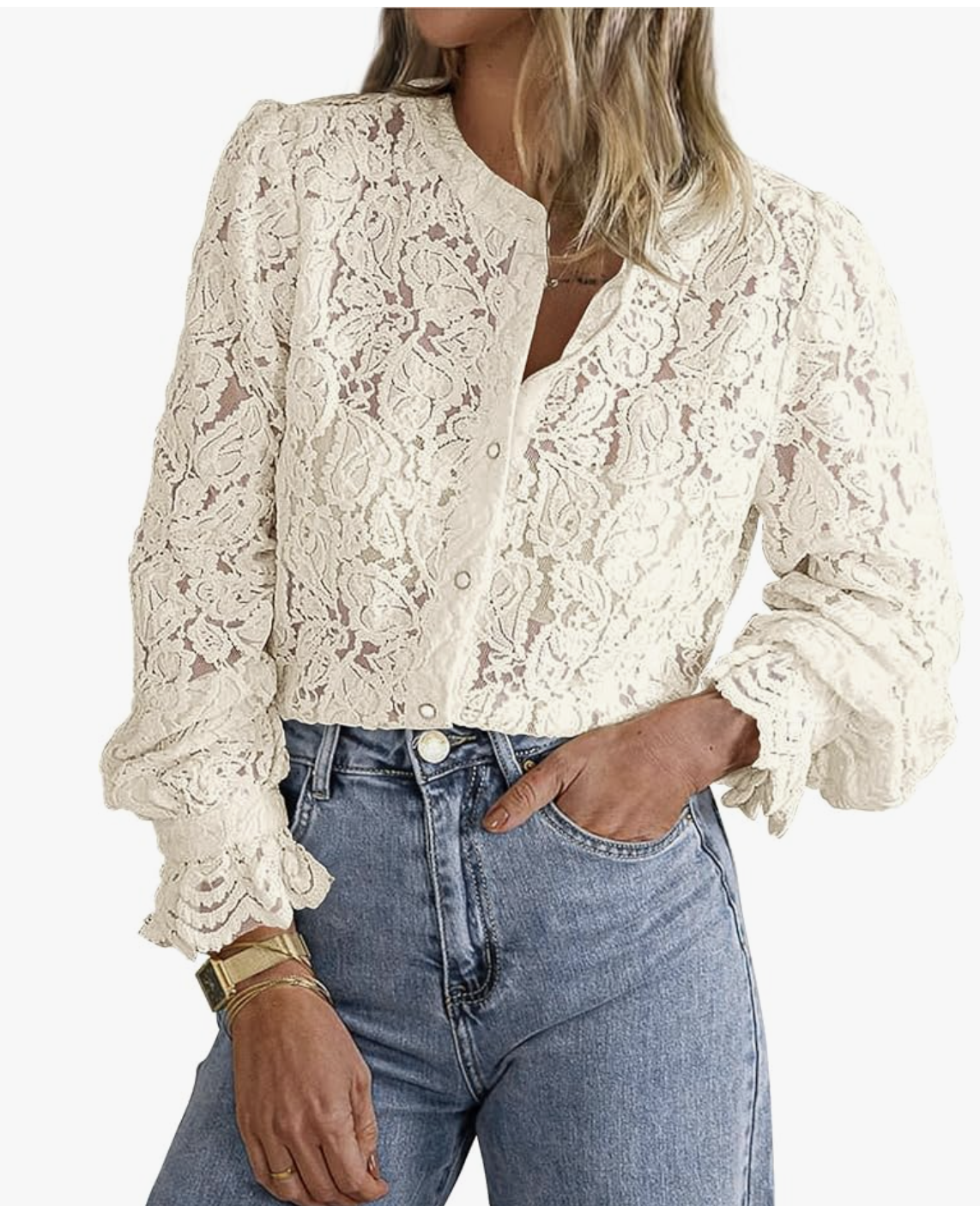A woman wearing a white long-sleeve sheer lace button-up shirt with a structured collar, tucked into blue denim jeans and styled with a gold watch and bracelets.