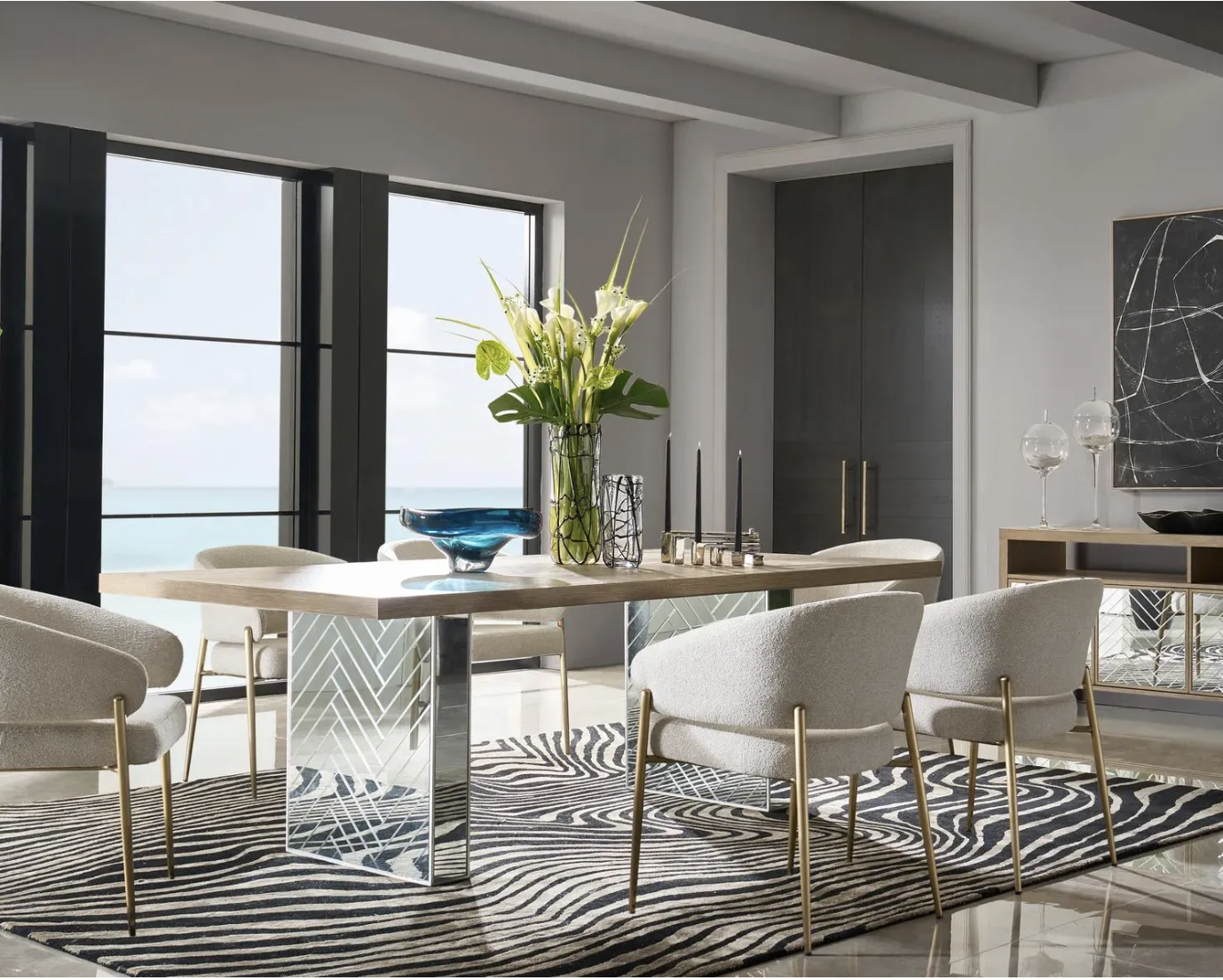 A modern dining room featuring a large zebra-print area rug under a contemporary glass dining table with brass accent legs and velvet chairs.