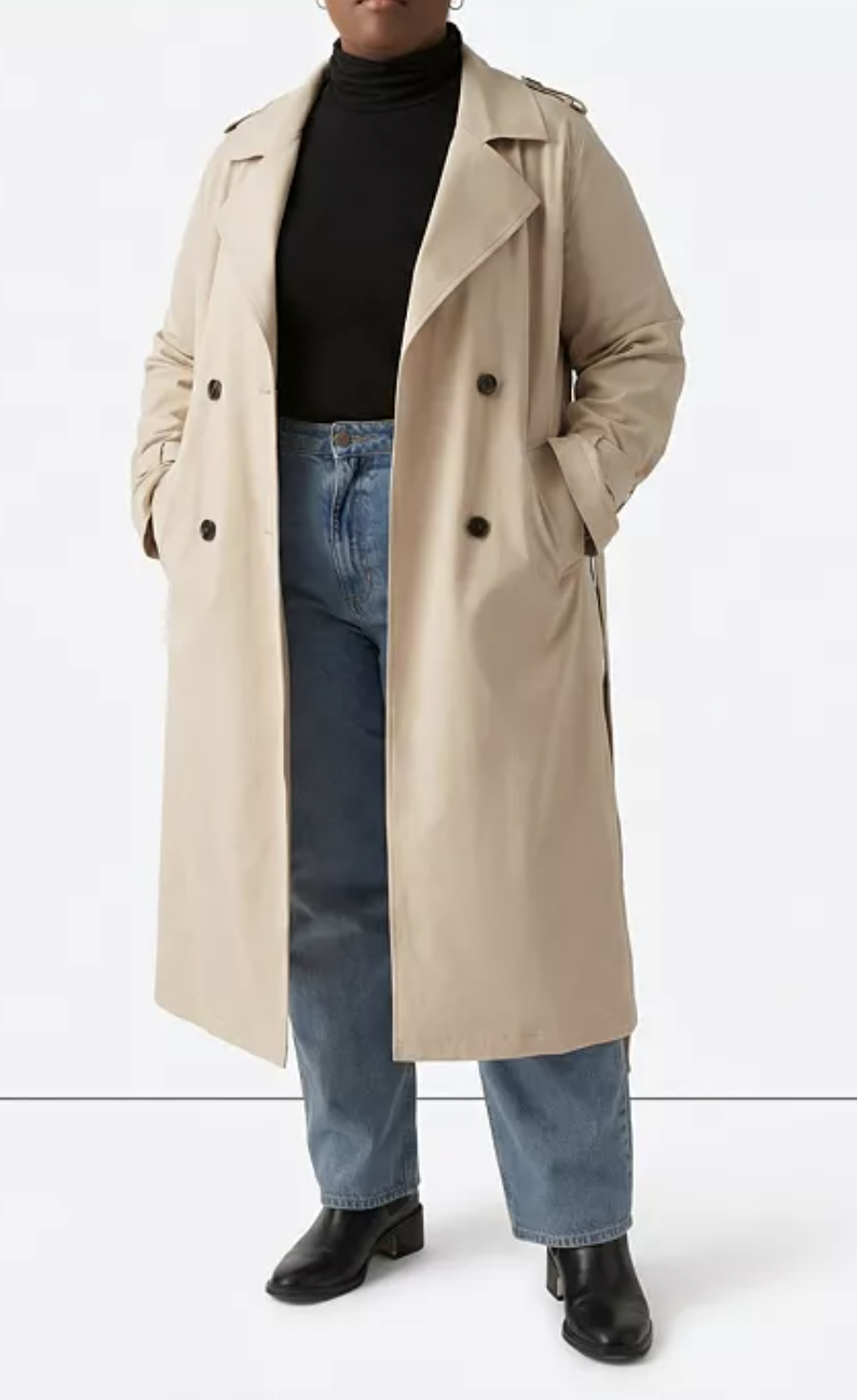 A woman wearing the tan Universal Standard Plus Size Park Soft Trench featuring a draped open-front, structured storm flaps, and a relaxed longline silhouette.